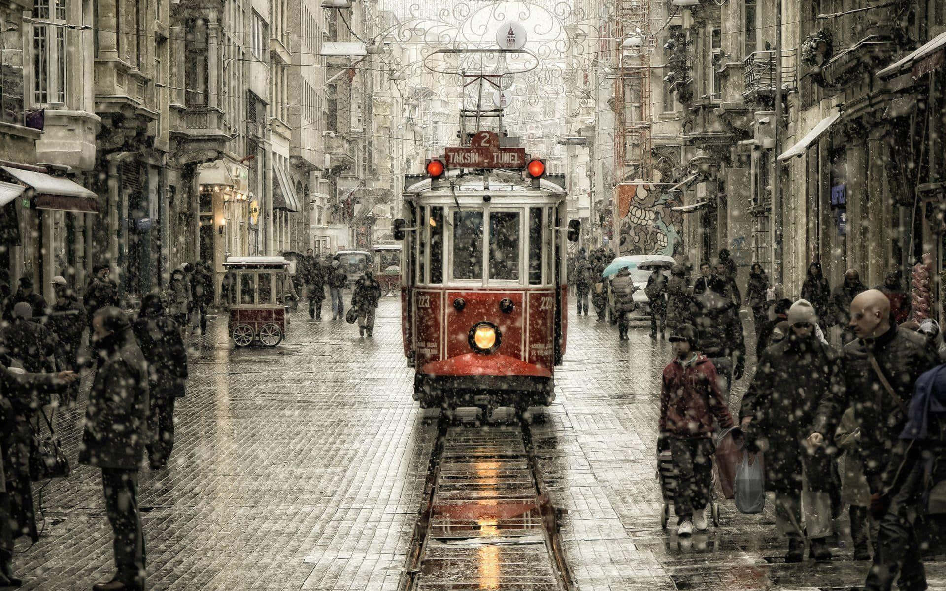 Winter Cityscape 桌布 壁紙 — 一輛紅色歷史電車在伊斯坦堡的雪街上滑行，行人們在飄雪中行走在濕漉漉的鵝卵石上。