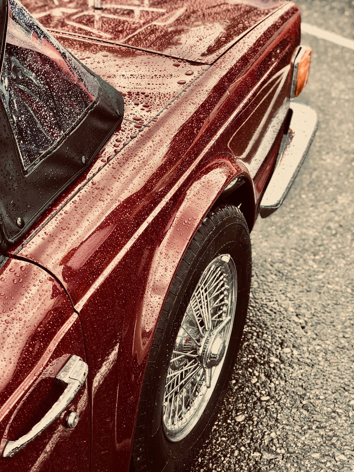 復古紅色敞篷車的特寫，引擎蓋和鋼絲輪圈上有雨滴。
