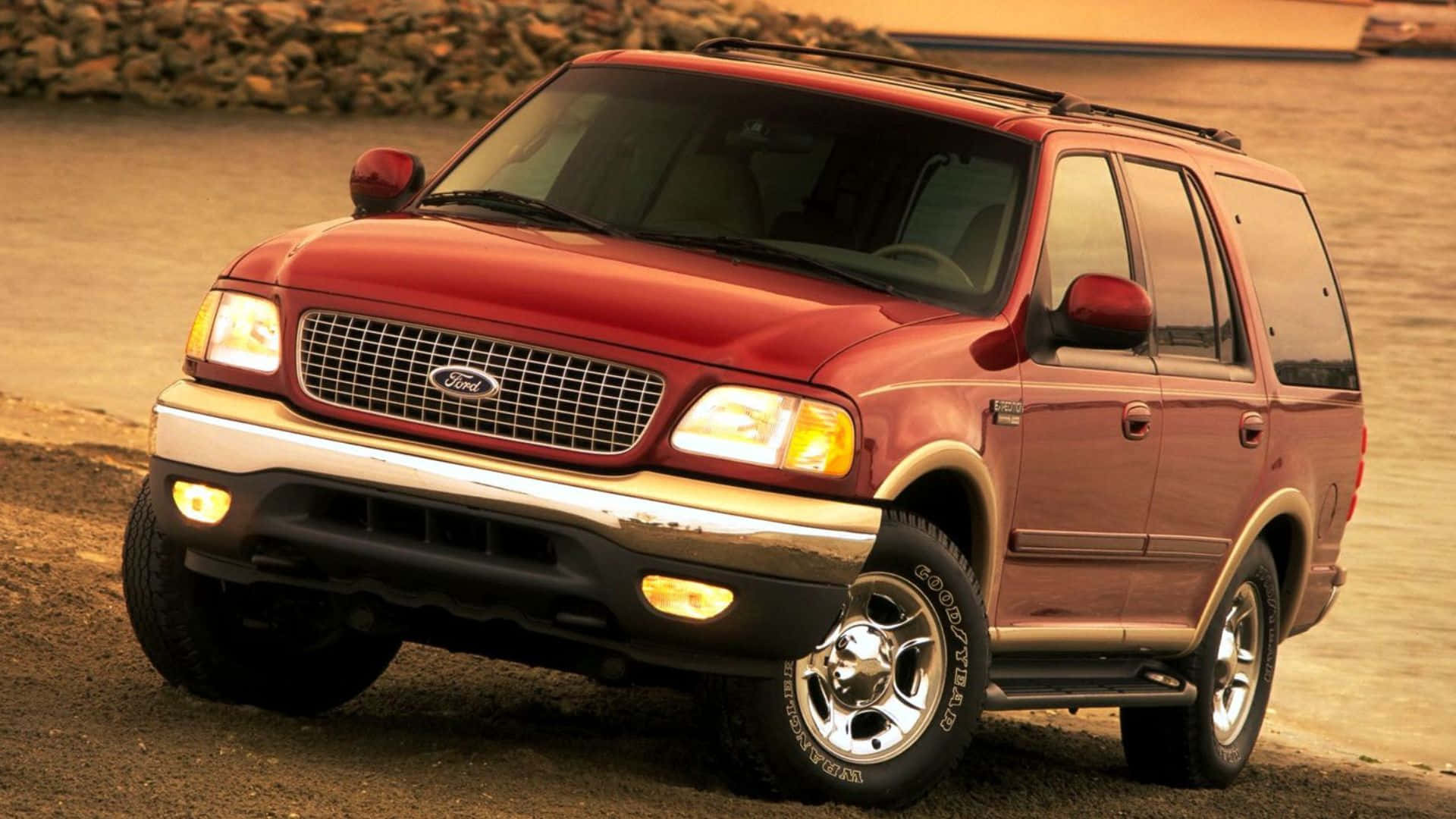 Ford Expedition 桌布 壁紙 — 一輛紅色福特 Explorer SUV 停泊在碎石路上，車頭燈亮起，沐浴在溫暖的金色黃昏光線中。