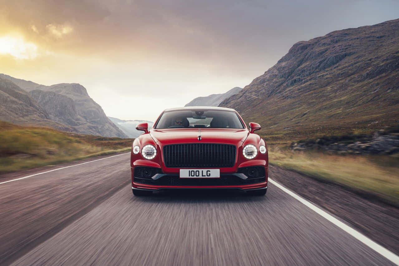 Bentley Flying Spur 桌布 壁紙 — 一輛紅色賓利 Continental GT 在日落時分沿著蜿蜒的山路疾馳，背景是模糊的動感和崎嶇的山峰。