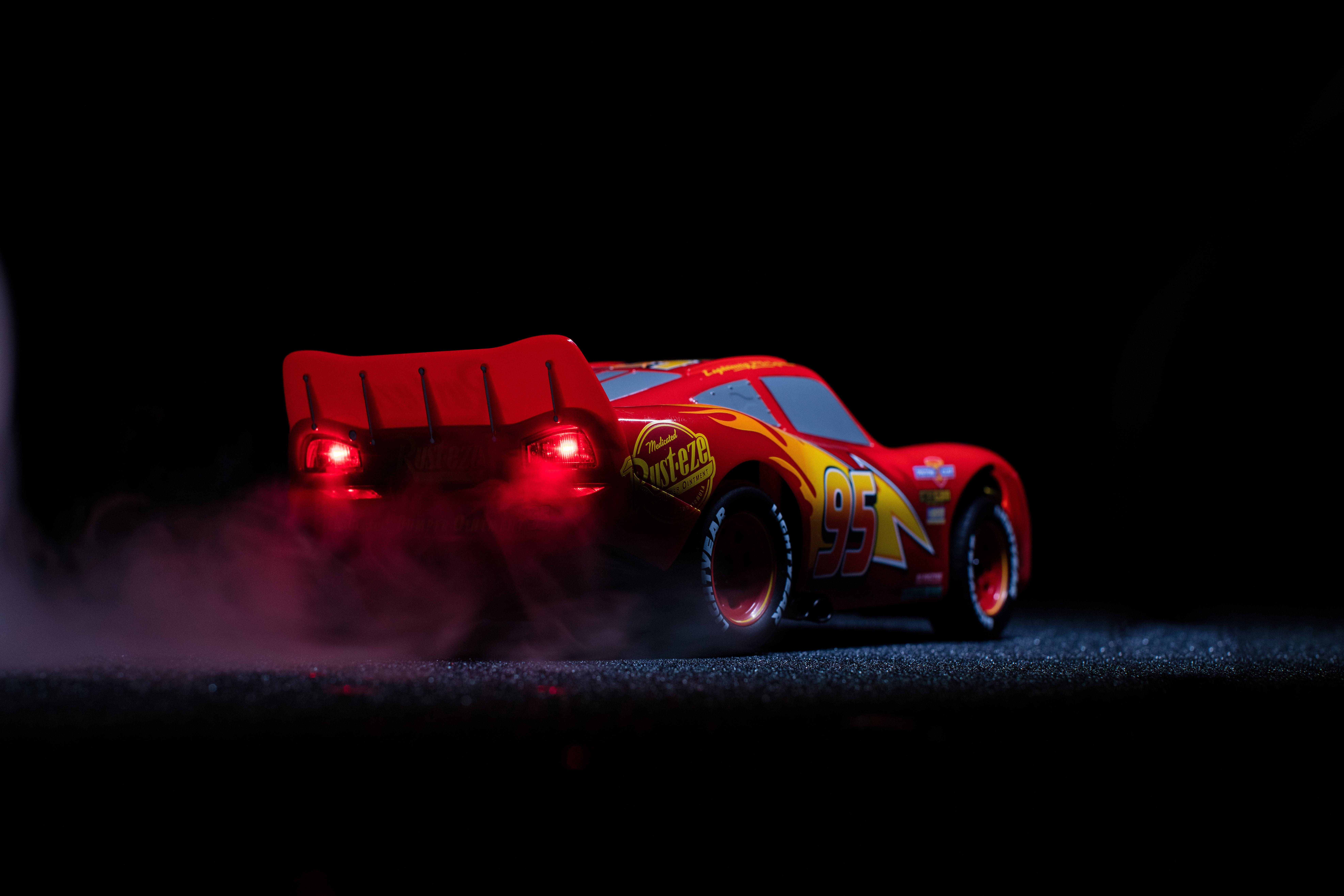 Sports Car 桌布 壁紙 — 一輛紅色閃電麥坤玩具車，帶有發光的尾燈，在深色瀝青表面上揚起煙霧。