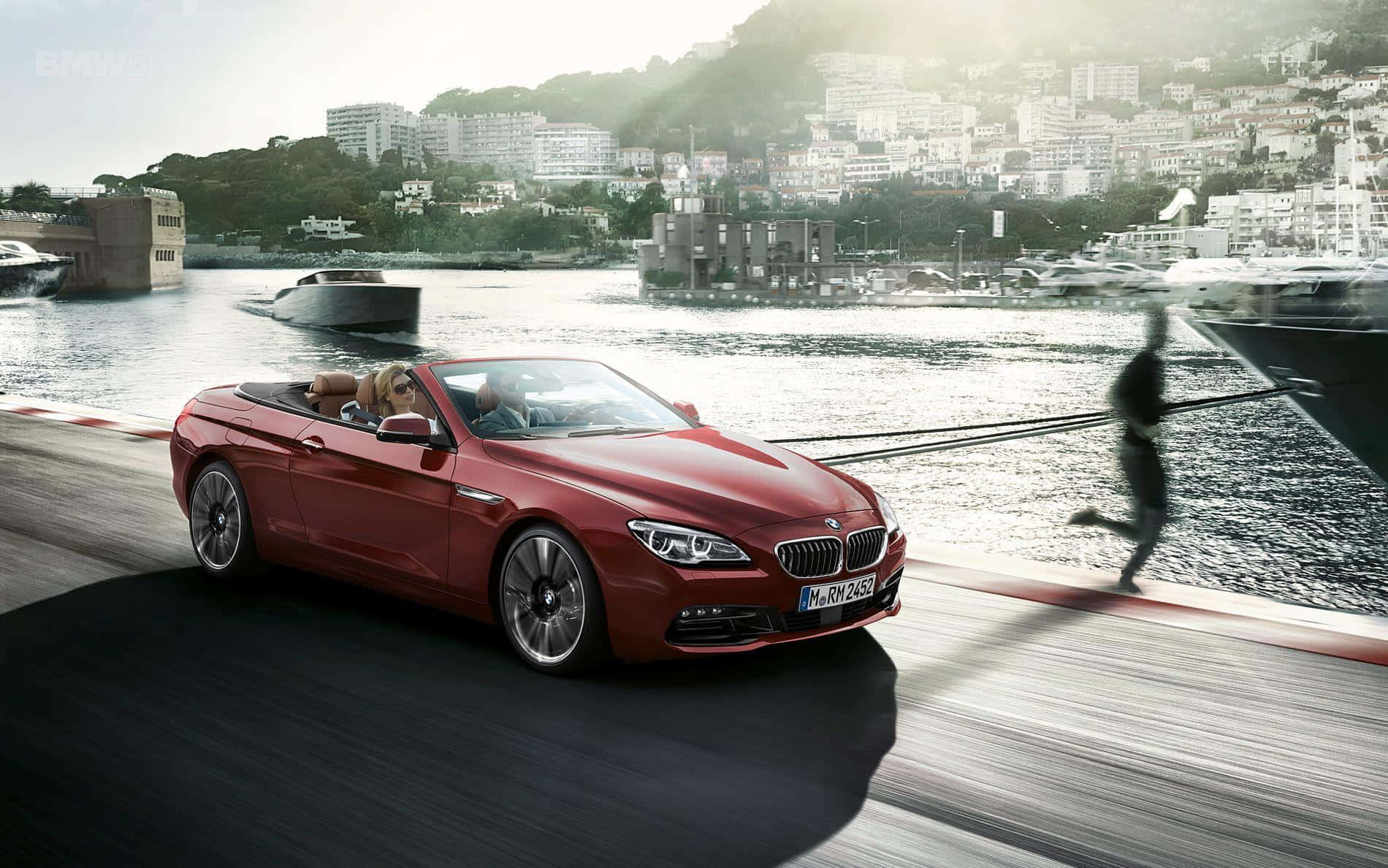 Bmw 6 Series 桌布 壁紙 — 一輛紅色開篷寶馬在海濱道路上飛馳，背景中有一個模糊的跑者和遊艇碼頭。