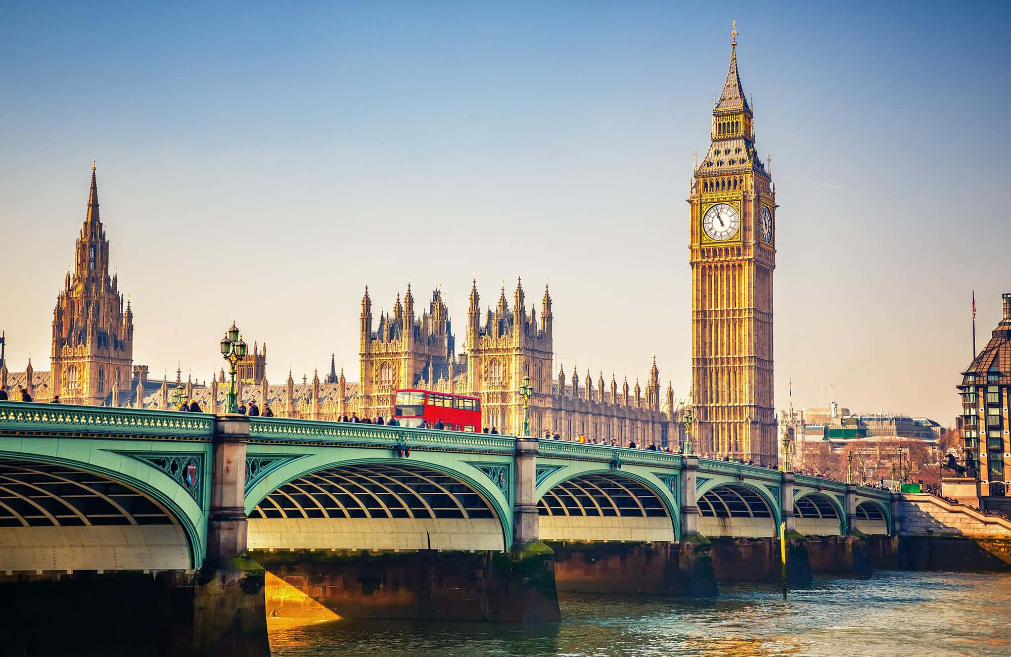 UK 桌布 壁紙 — 一輛紅色雙層巴士在黃金時段駛過綠色的橋，橋下是標誌性的伊麗莎白塔和哥德式的威斯敏斯特宮。