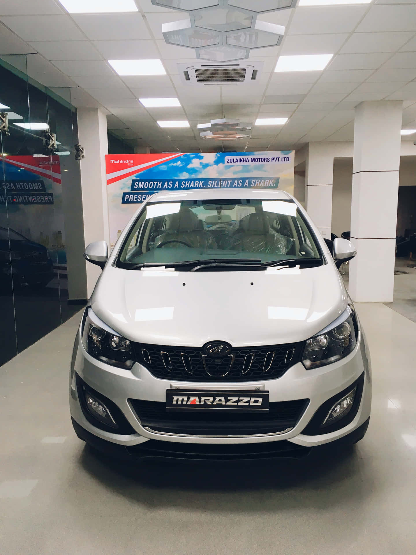  壁紙 — 一輛純白色的 Marazzo 汽車在明亮現代的經銷商展廳中展示，地板反射光線，並掛有品牌橫幅。