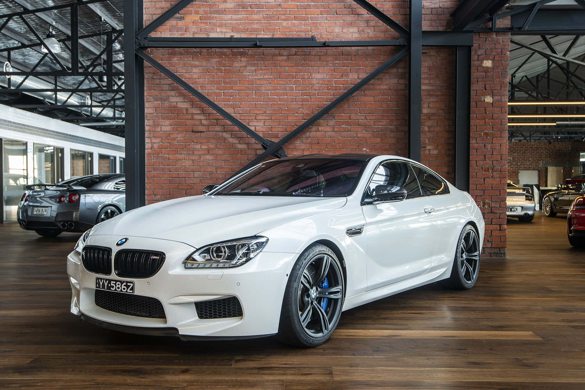 Bmw M6 桌布 壁紙 — 一輛純白色的BMW M6轎跑車在寬敞的磚牆木地板車庫中，在明亮的燈光下閃閃發光。