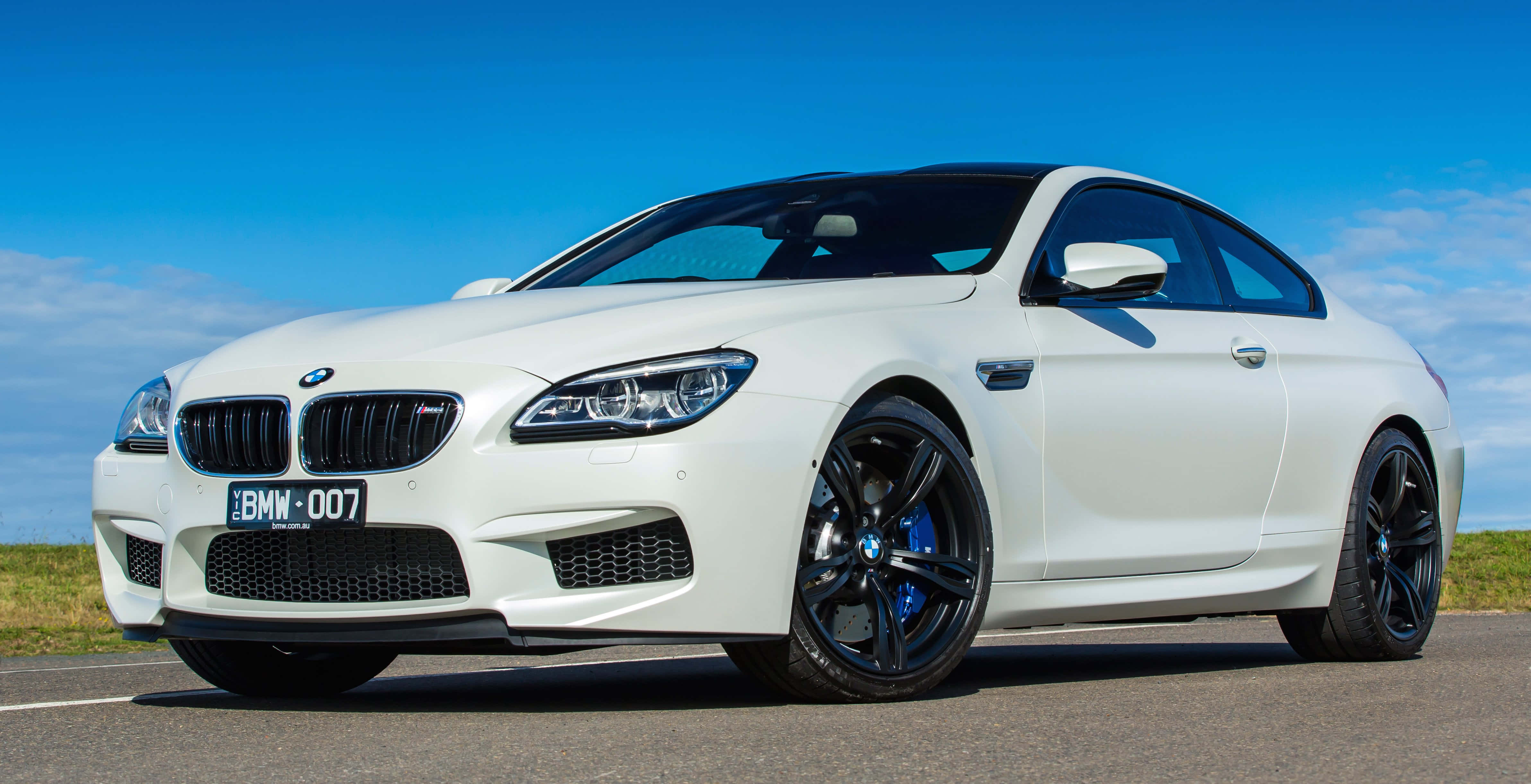 Bmw M6 桌布 壁紙 — 一輛純白色的BMW M6雙門轎跑車，配備黑色輪圈和藍色制動卡鉗，停在晴朗藍天下的瀝青路上。