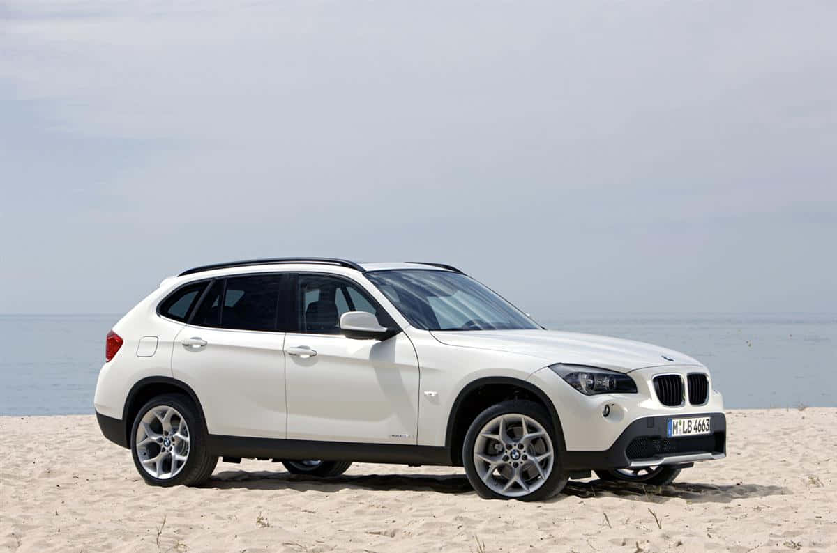 Bmw I8 桌布 壁紙 — 一輛純白色的BMW X1 SUV停泊在沙灘上，背景是平靜的海洋和陰天。