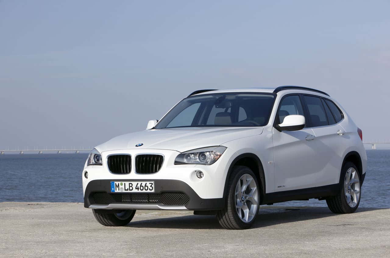 Bmw X1 桌布 壁紙 — 一輛純白色的BMW X1 SUV停泊在混凝土碼頭上，俯瞰著晴朗天空下平靜的藍色海水。