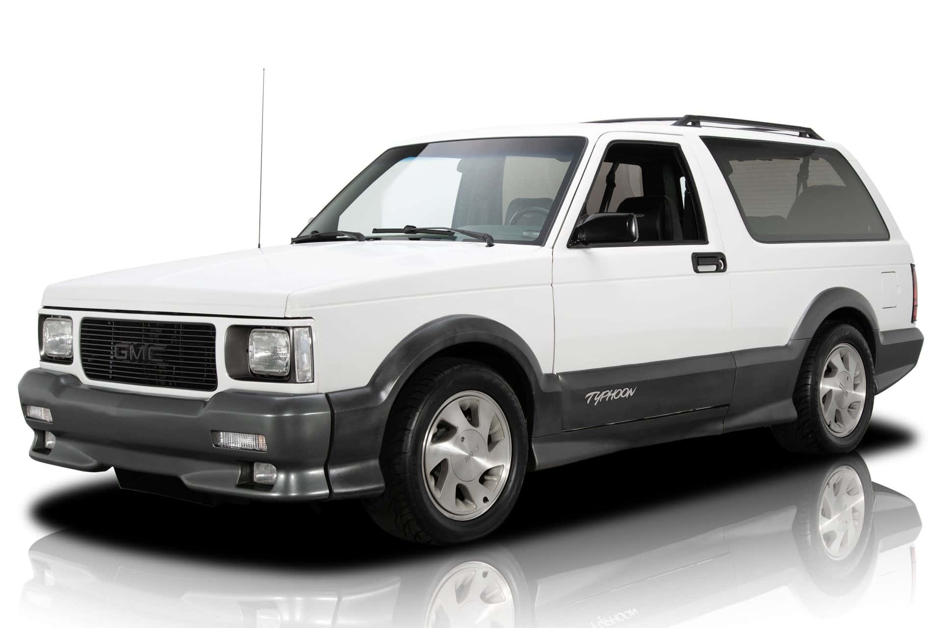 Gmc Typhoon 桌布 壁紙 — 一輛純白色的GMC Typhoon SUV，帶有黑色飾邊和銀色輪圈，站在反射的攝影棚地板上，背景是乾淨的白色。