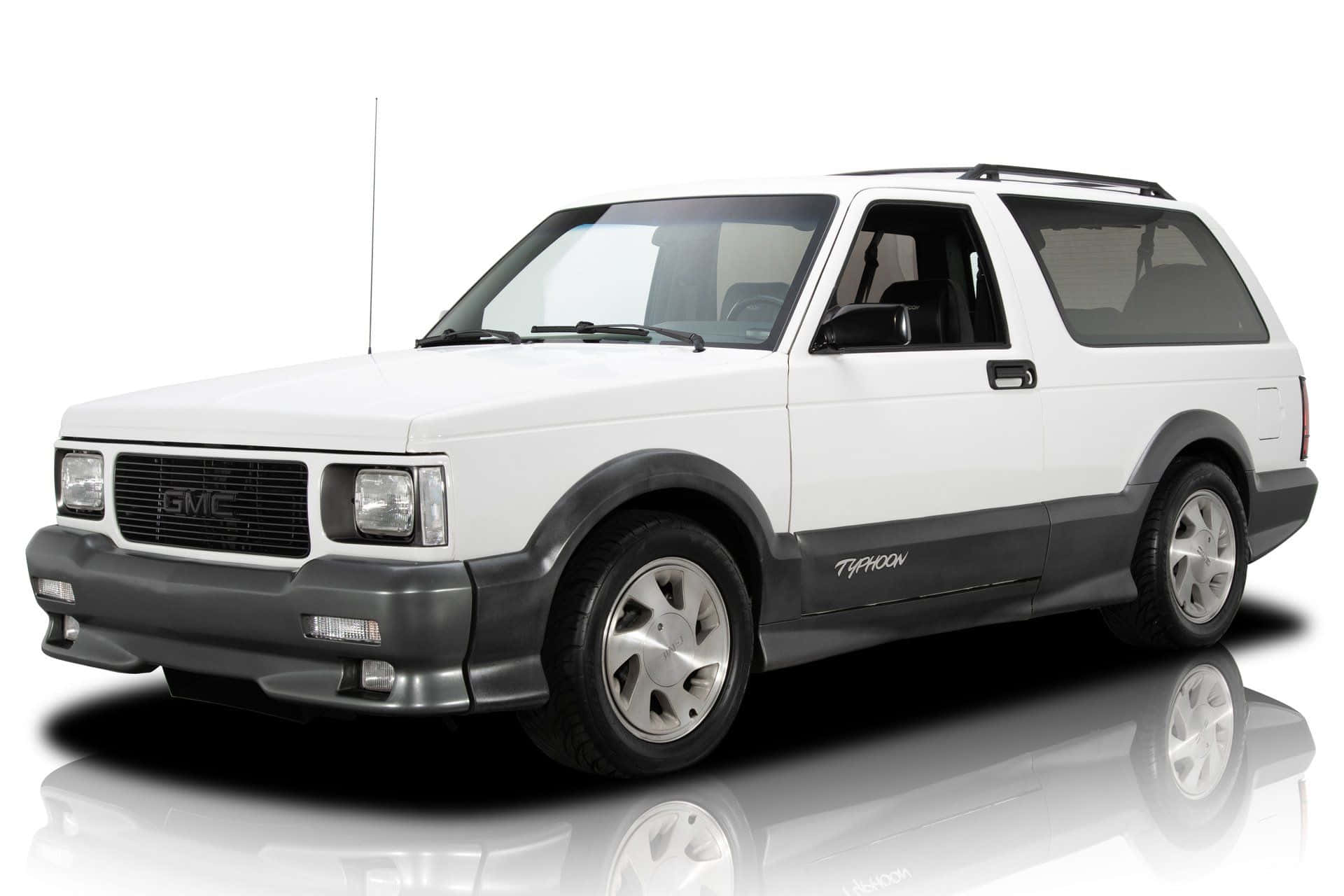 Gmc Typhoon 桌布 壁紙 — 一輛純白色的GMC Typhoon SUV，帶有黑色飾邊和銀色輪圈，站在反射的攝影棚地板上，背景是乾淨的白色。