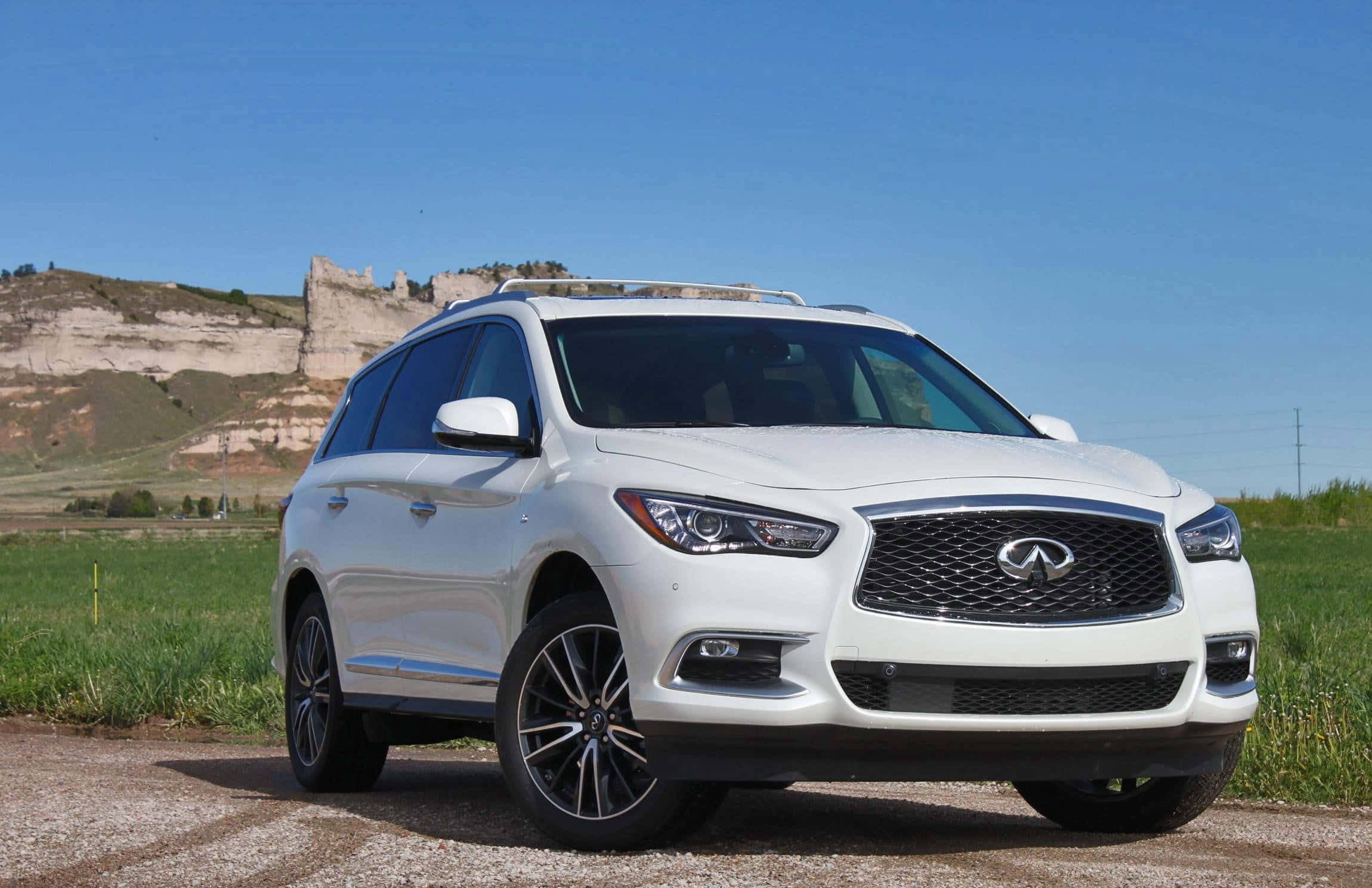 Infiniti Qx60 桌布 壁紙 — 一輛純白色的Infiniti SUV停泊在碎石路上，背景是壯麗的懸崖和清澈的藍天。