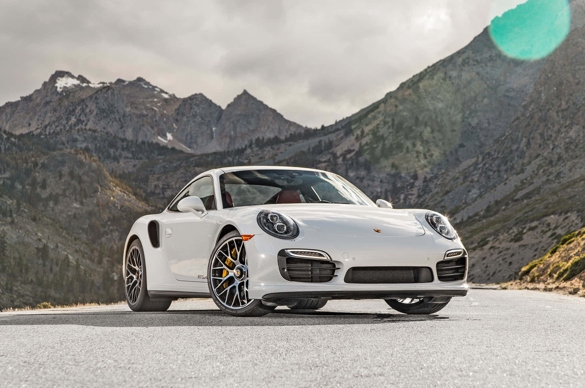 保時捷 桌布 壁紙 — 一輛純白色的保時捷911 Turbo S在山路上閃閃發光，背景是白雪覆蓋的山峰和陰天。