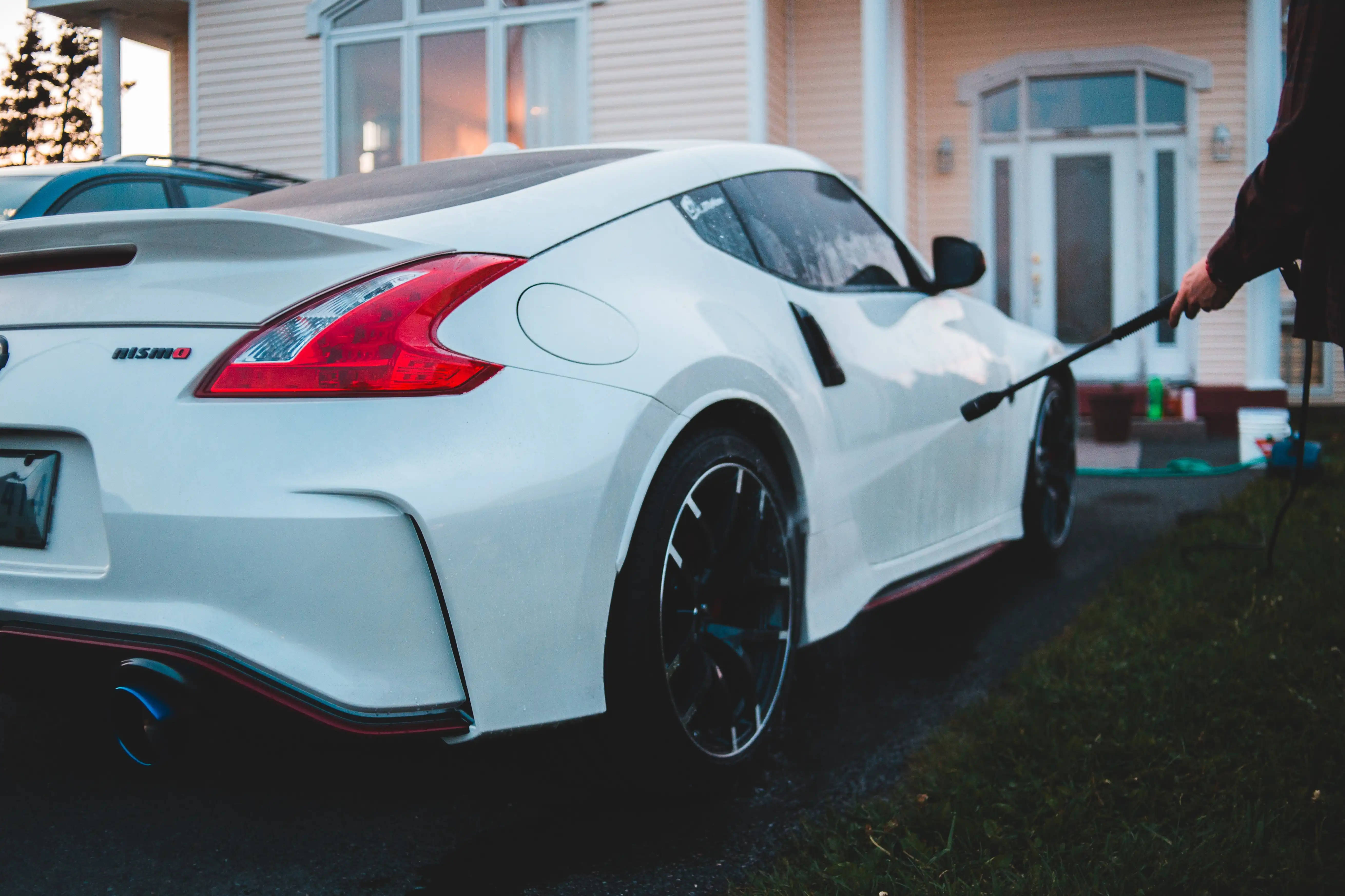 Nissan 桌布 壁紙 — 一輛純白色的日產370Z Nismo在黃昏時分於郊區房屋前用水喉清洗。