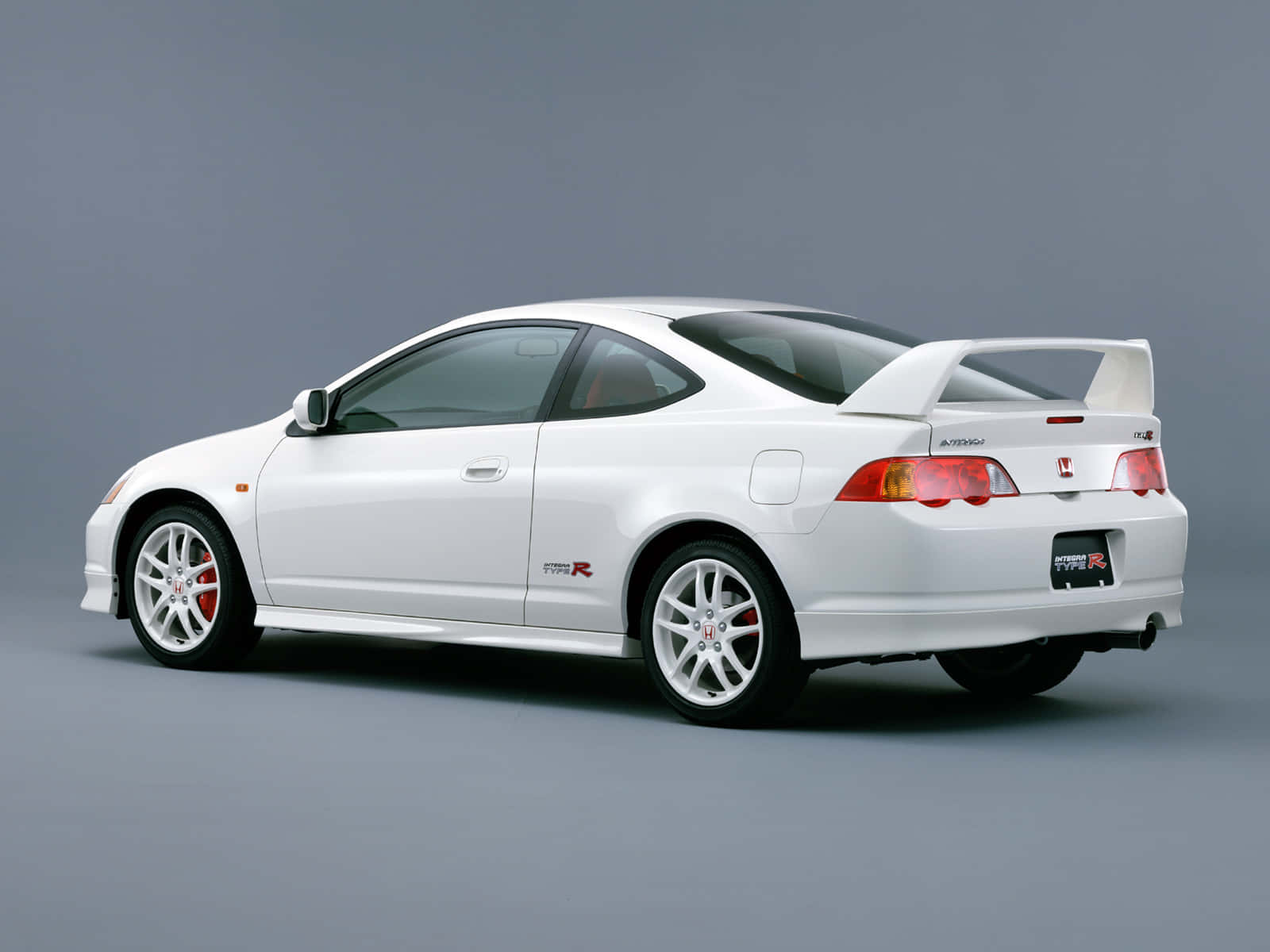 Honda Integra 桌布 壁紙 — 一輛純白色的本田 CR-R 運動轎跑車，配備紅色制動卡鉗和後擾流板，在簡約的工作室環境中展示。