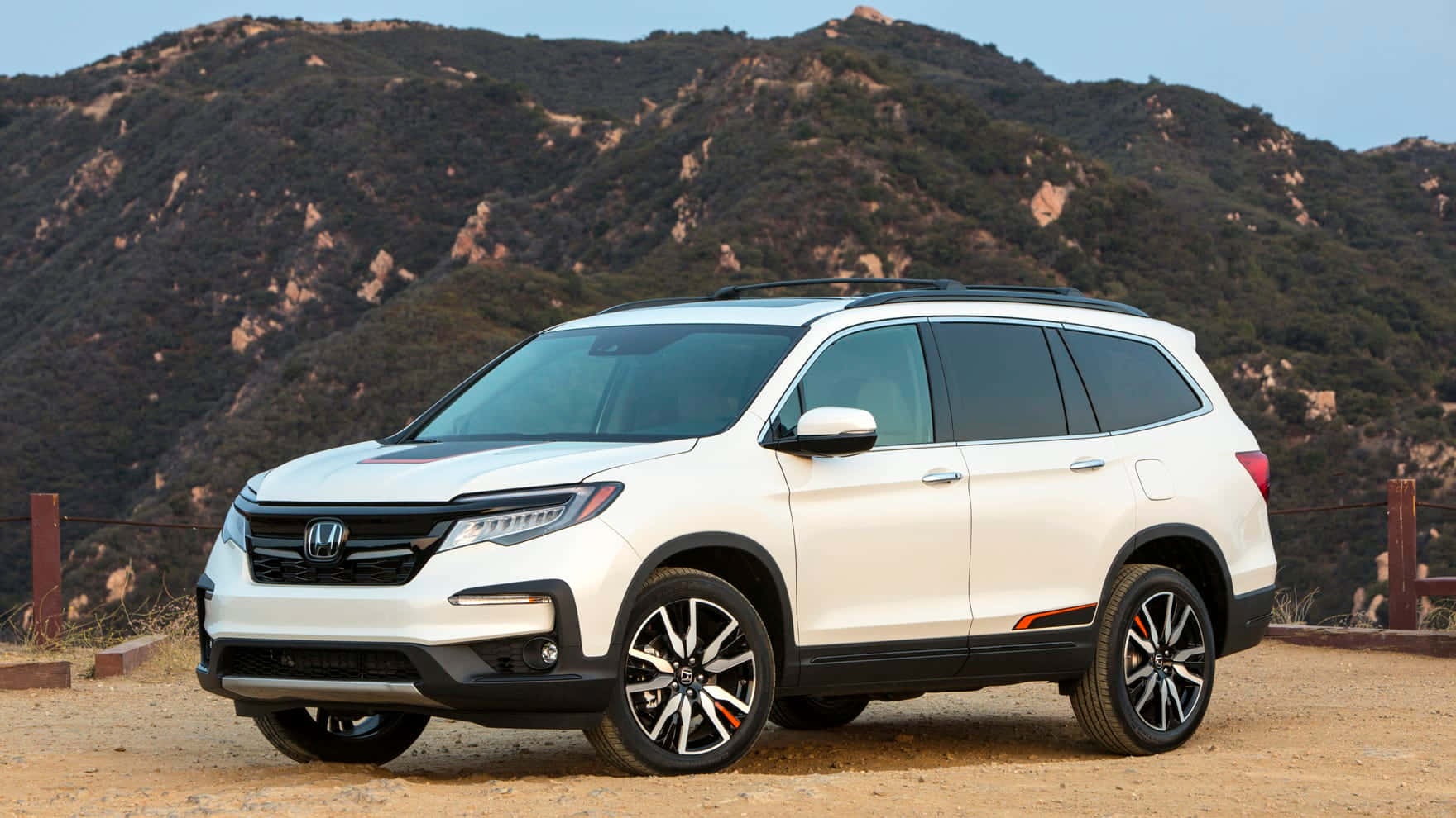 Honda Pilot 桌布 壁紙 — 一輛純白色的本田Pilot SUV停泊在塵土飛揚的地形上，背景是崎嶇的山脈和清澈的藍天。