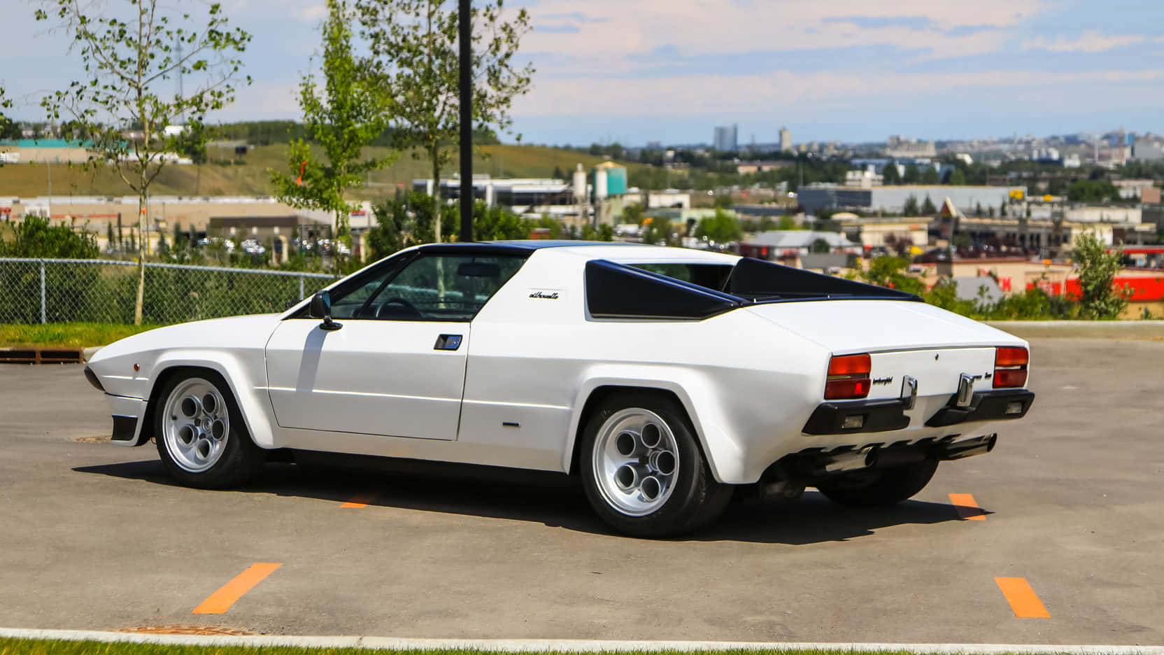 Lamborghini Silhouette 桌布 壁紙 — 一輛純白色的林寶堅尼 Jalpa 跑車停泊在陽光普照的城市地段，背景是城市天際線。