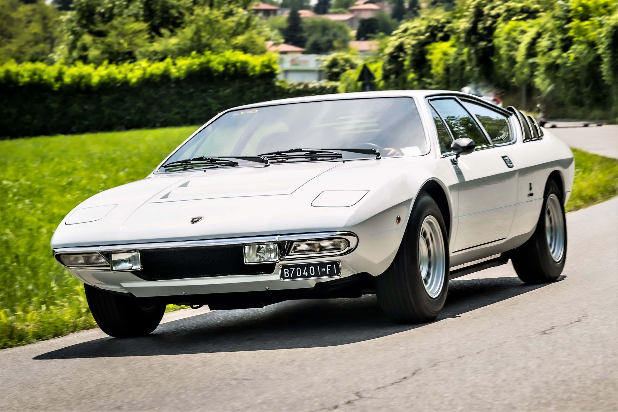Lamborghini Urraco 桌布 壁紙 — 一輛純白色的林寶堅尼 Marzal 在陽光明媚的鄉村道路上巡航，兩旁是茂密的綠色樹籬和樹木。