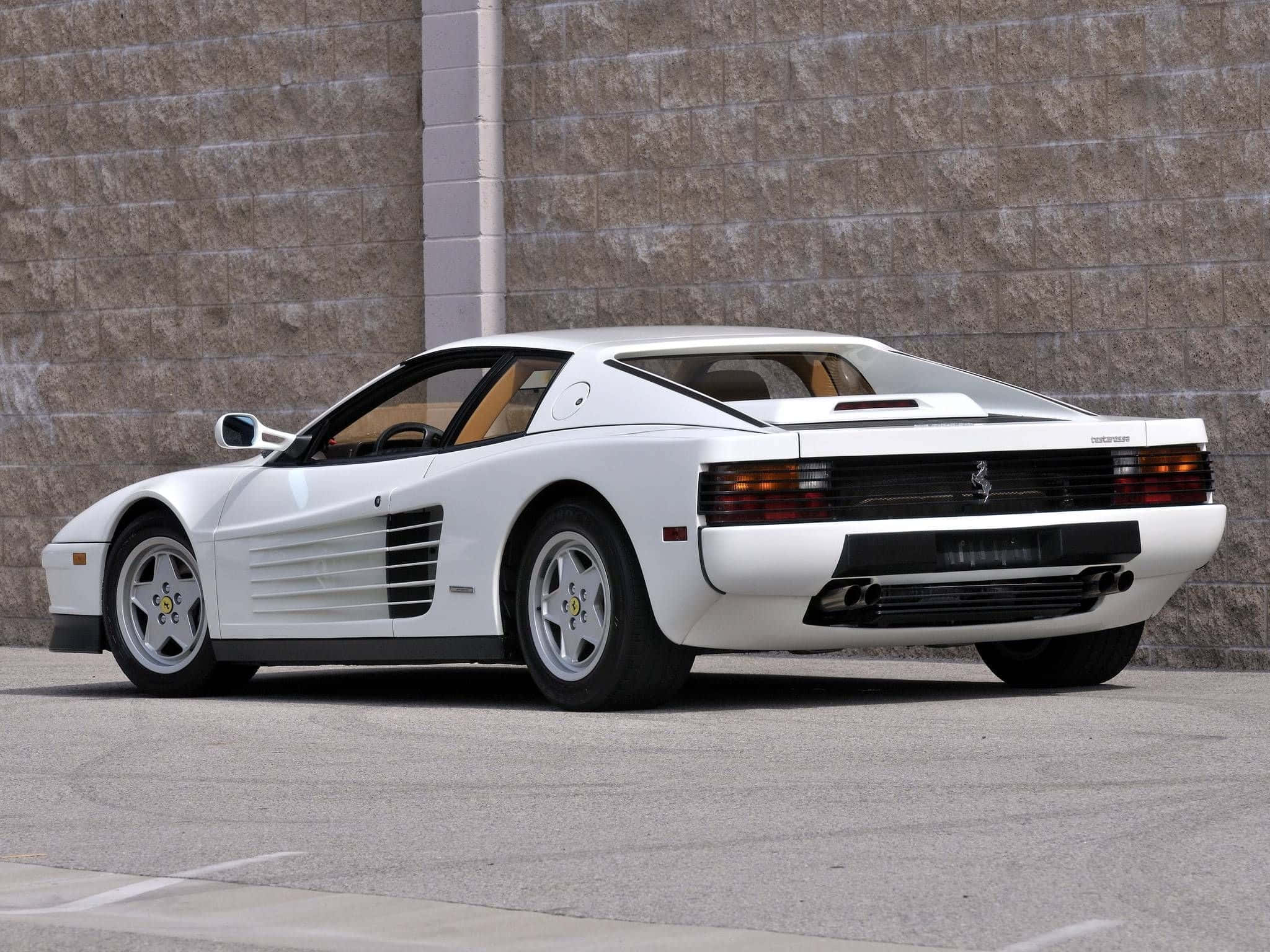 Ferrari Testarossa 桌布 壁紙 — 一輛純白色的法拉利 Testarossa 以傾斜角度停泊在質感石牆旁，地面為鋪砌路面。