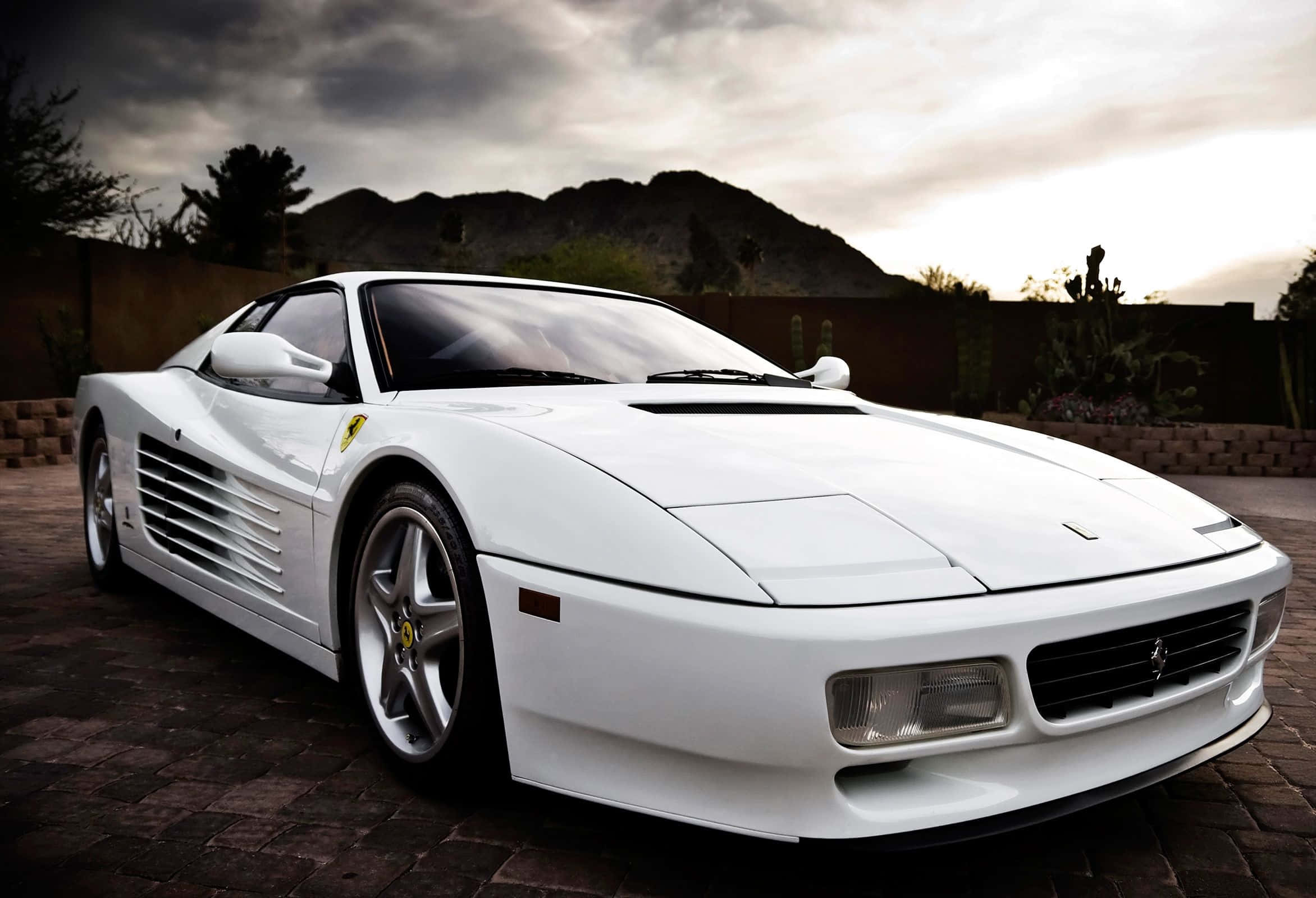 Ferrari Testarossa 桌布 壁紙 — 一輛純白色的法拉利跑車在戲劇性的暮色天空下，以沙漠山脈為背景閃閃發光。