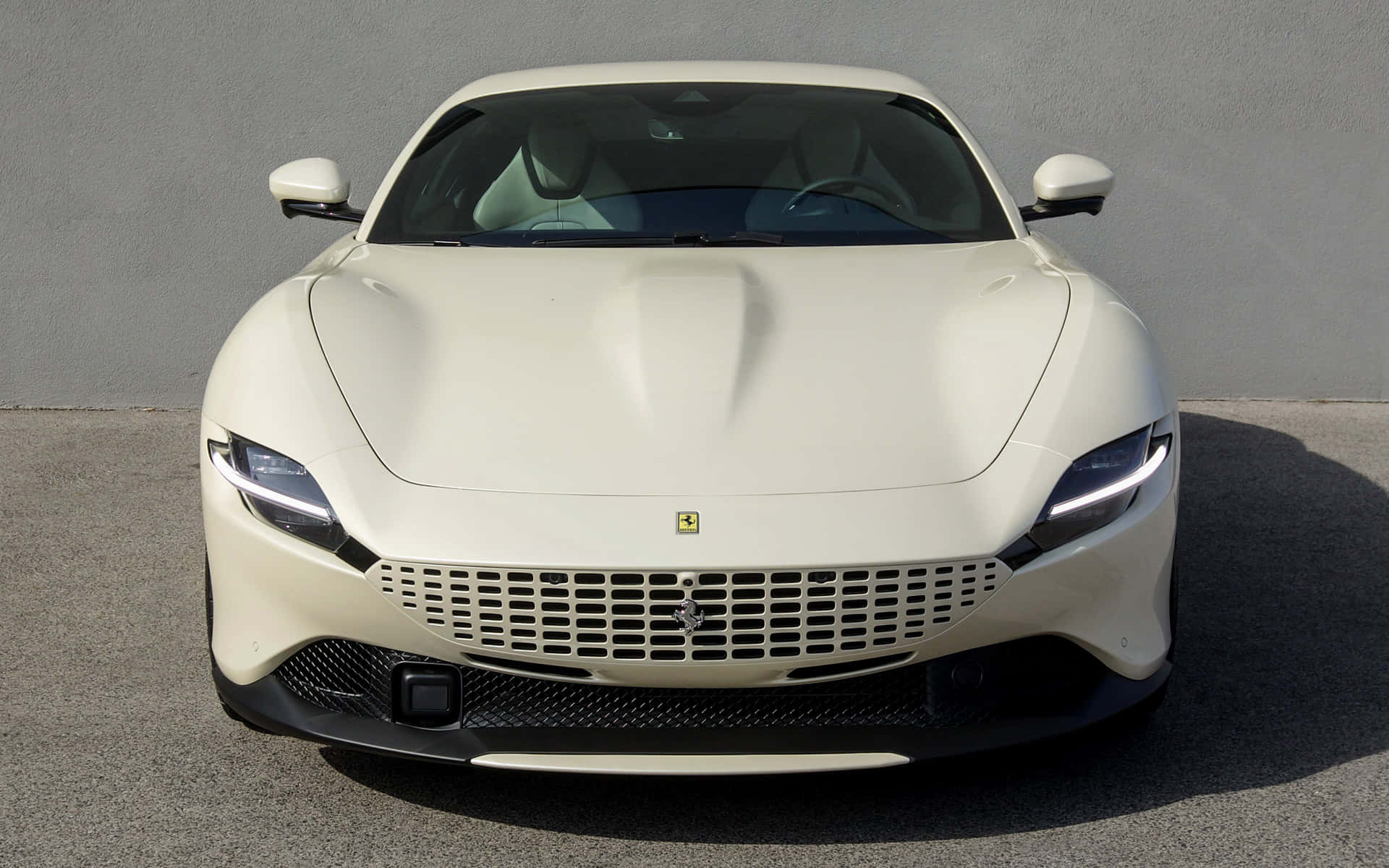 Ferrari Roma 桌布 壁紙 — 一輛純白色的法拉利跑車在明亮的日光下，正面朝向一面樸素的灰色牆壁。