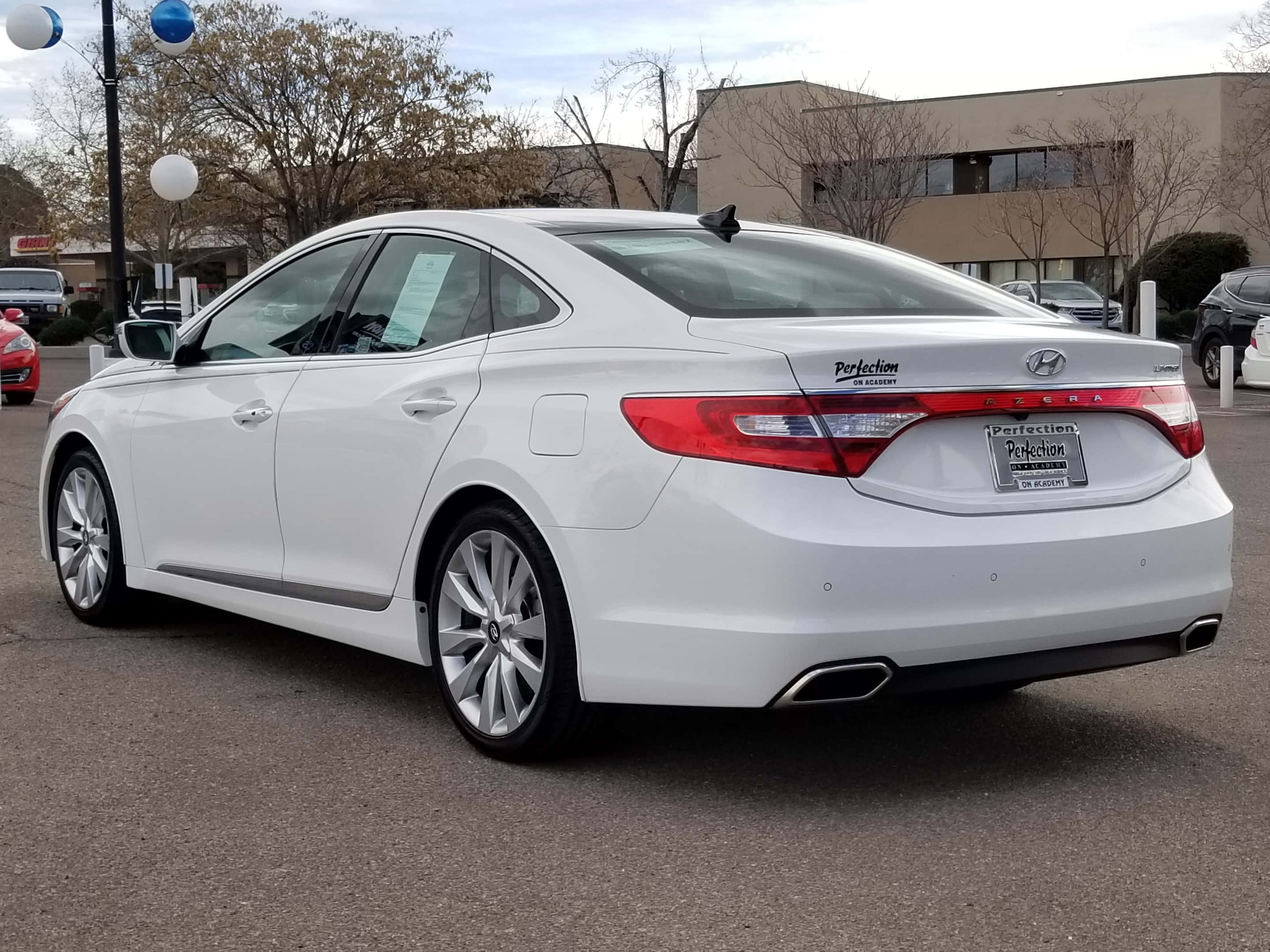 Hyundai Azera 桌布 壁紙 — 一輛純白色的現代轎車停放在經銷商場地，周圍有光禿禿的樹木和陰天。