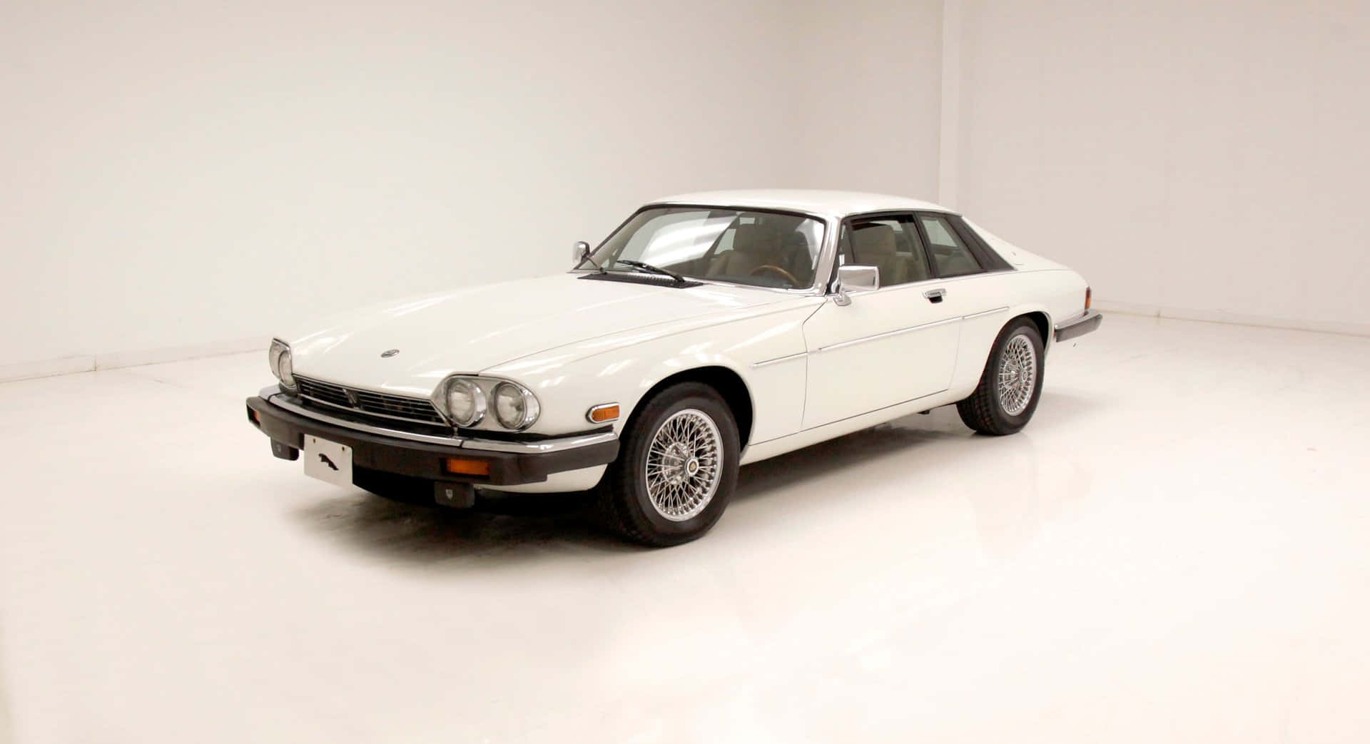 Jaguar Xjs 桌布 壁紙 — 一輛純白色的經典積架XJ-S轎跑車在明亮的影樓燈光下，在無縫的白色地板上閃閃發光。