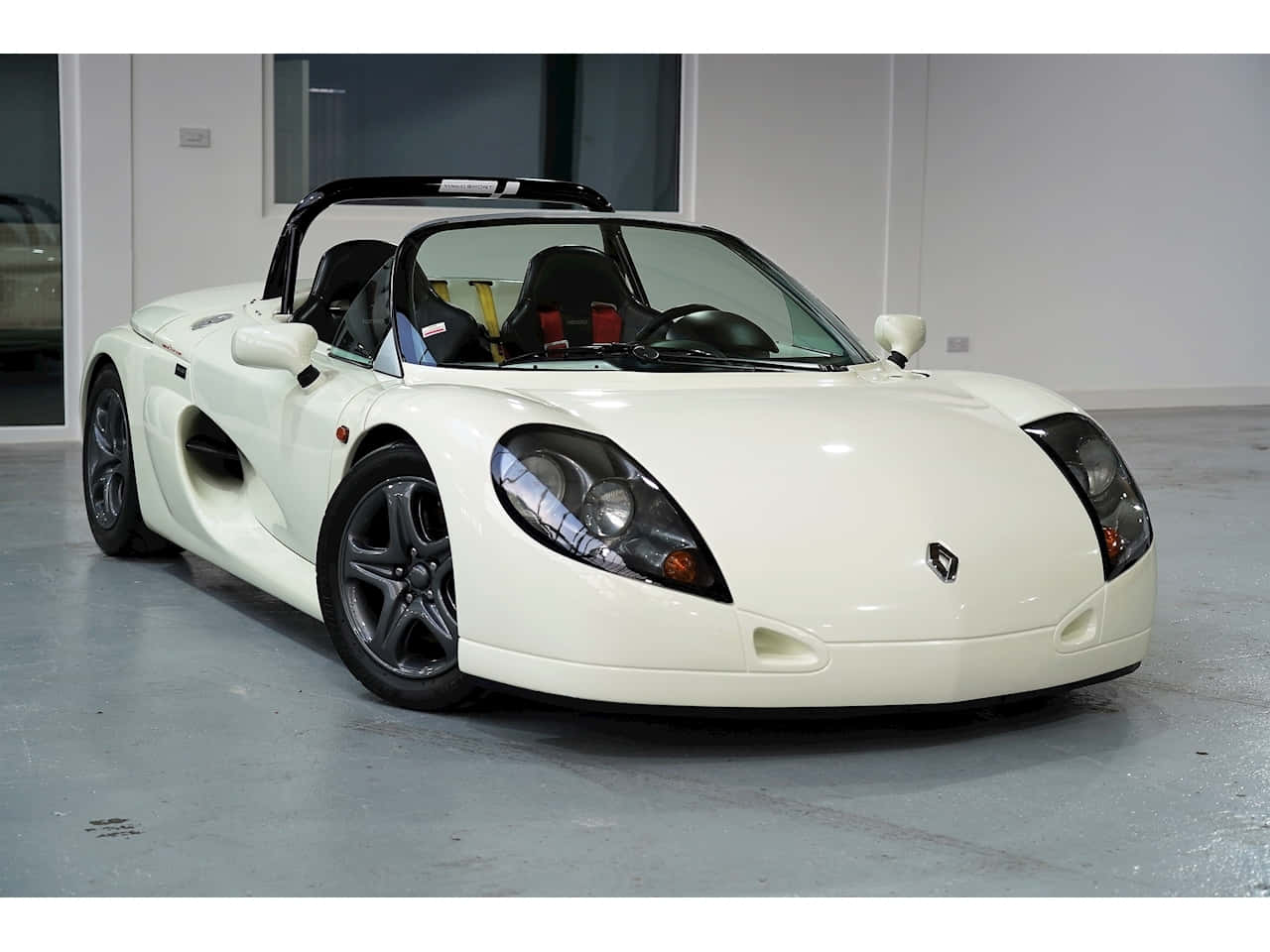 Renault Sport Spider 桌布 壁紙 — 一輛純白色的雷諾Spider跑車，帶有黑色飾邊和紅色安全帶，停放在簡約的室內車庫中。