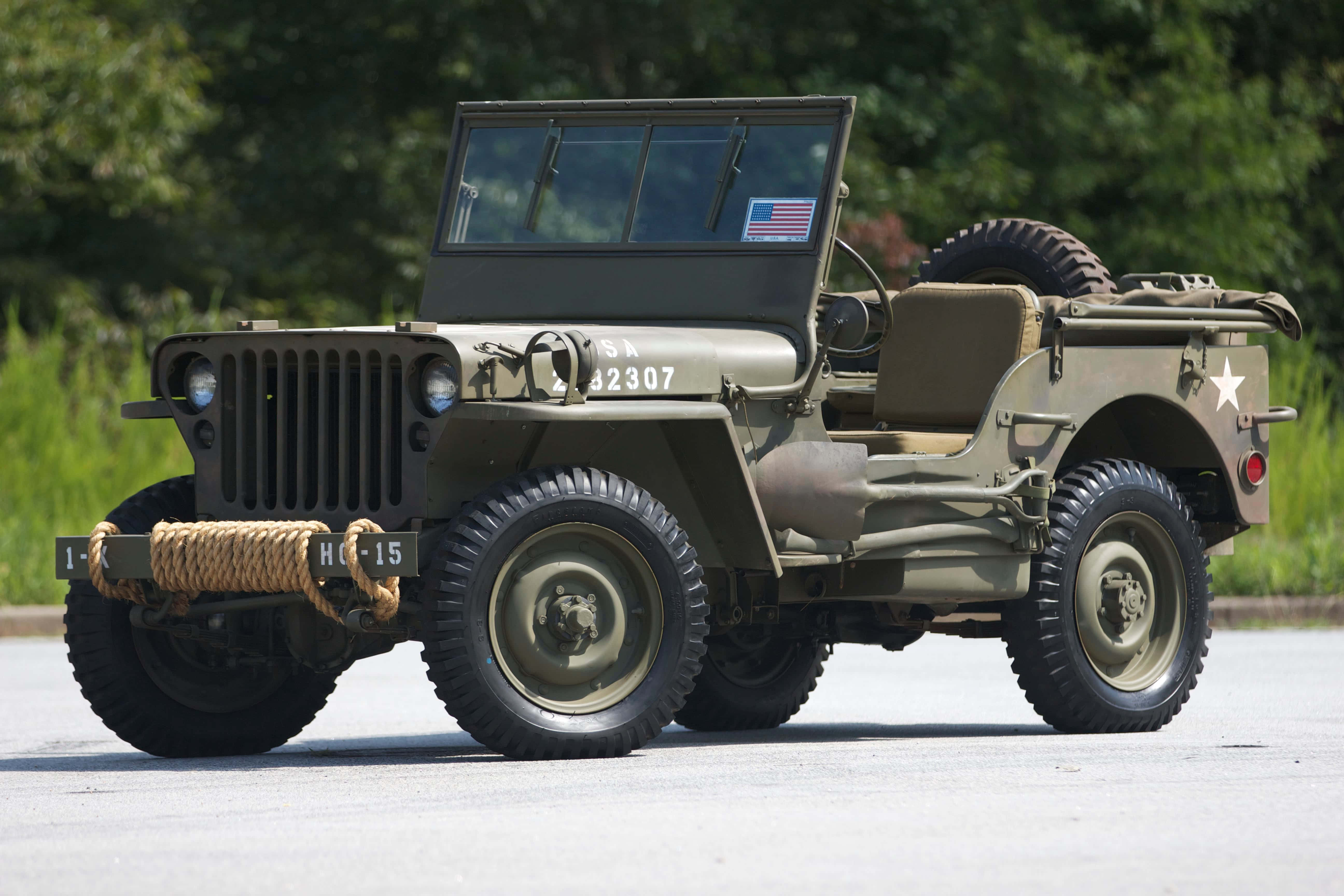 Jeep Willys 桌布 壁紙 — 一輛經典橄欖綠軍用吉普車，帶有星形徽章和繩索保險槓，在明亮的日光下停在路面上。