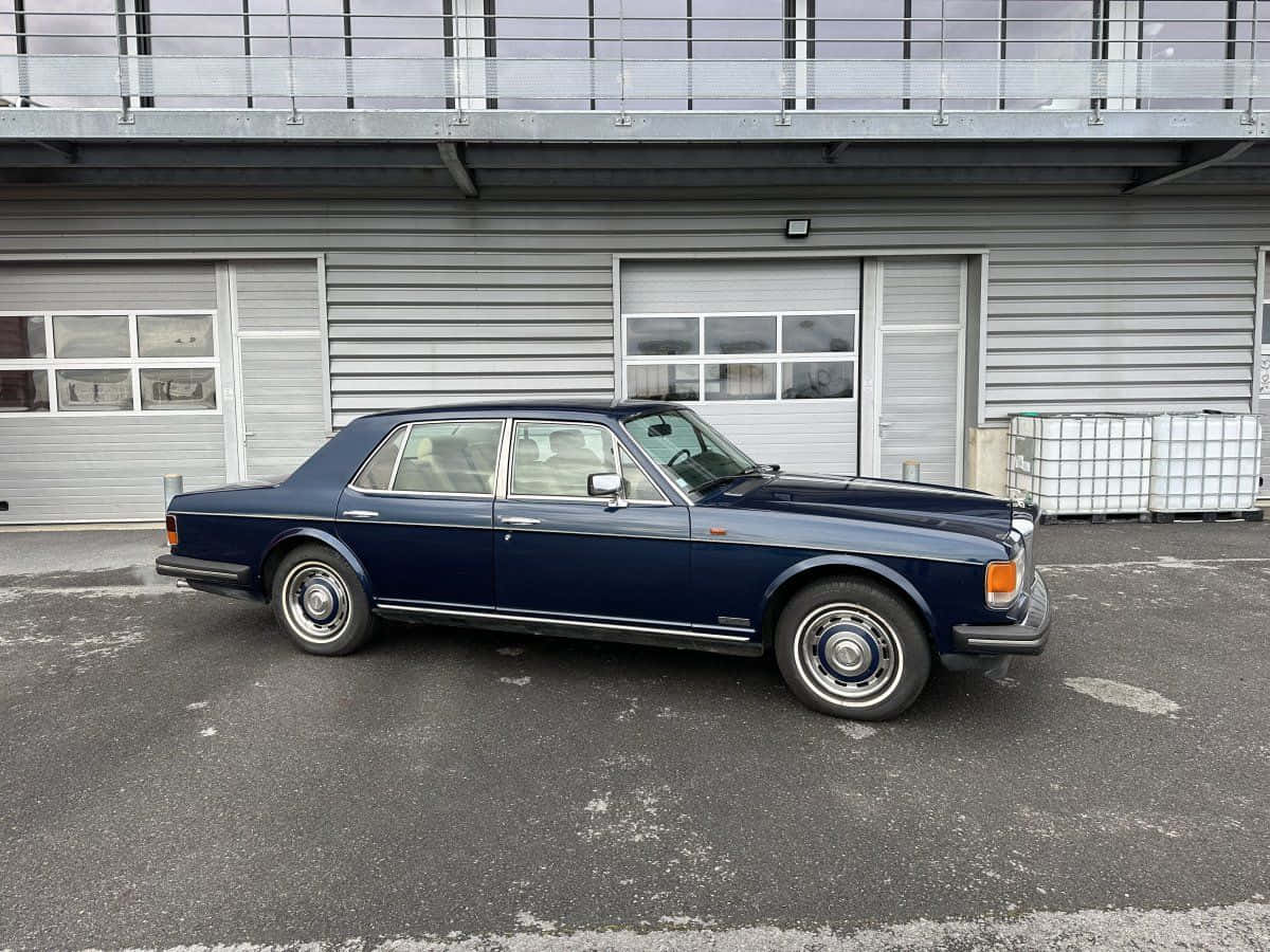 Bentley Eight 桌布 壁紙 — 一輛經典的海軍藍色勞斯萊斯優雅地停在一棟帶有灰色牆板和車庫門的現代工業建築前。