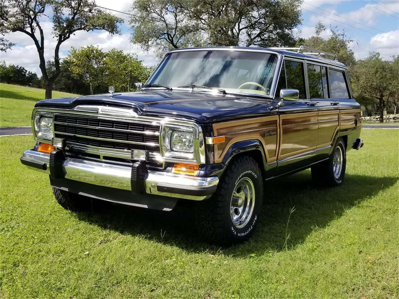 Jeep Wagoneer 桌布 壁紙 — 一輛經典的藍色木紋吉普切諾基旅行車停在茂密的綠草地上，天空部分多雲。