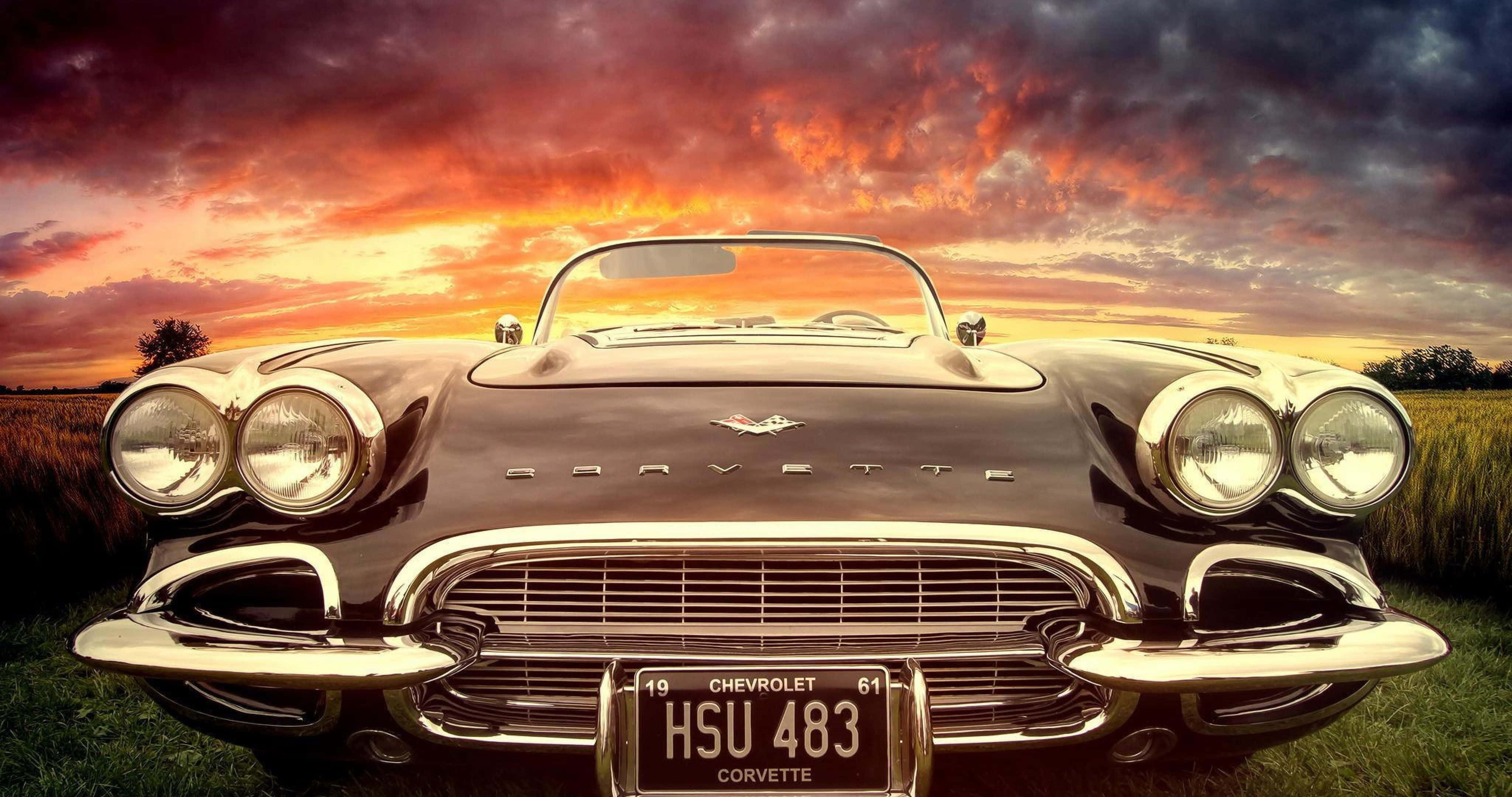 classic 桌布 壁紙 — 一輛經典的黑色1959年雪佛蘭Corvette敞篷車在橙紫色雲彩的熾熱日落天空下閃閃發光。