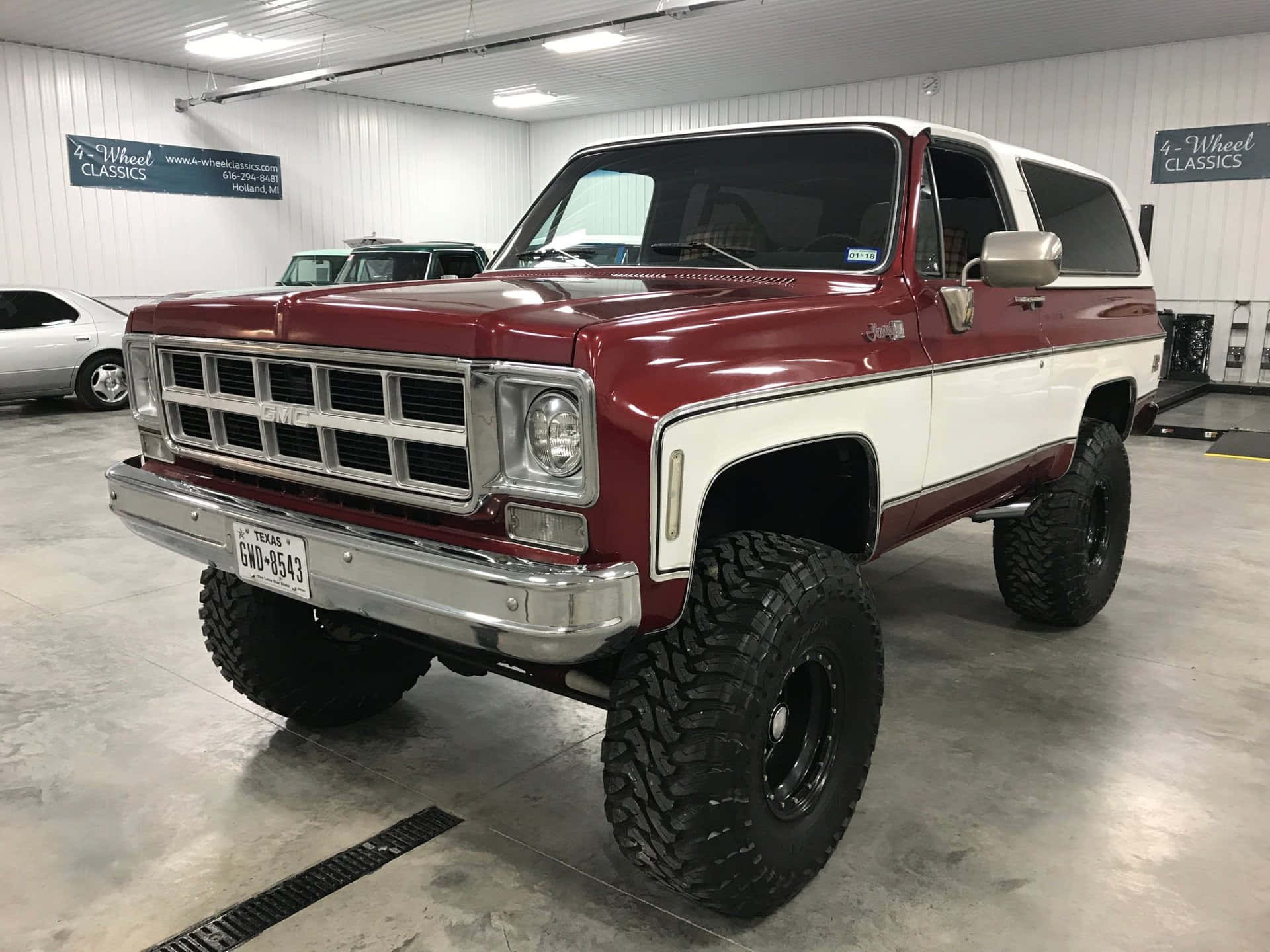 Gmc Jimmy 桌布 壁紙 — 一輛經典紅白配色的升高GMC Jimmy，配備超大輪胎，自豪地停放在光線充足的室內展廳中。
