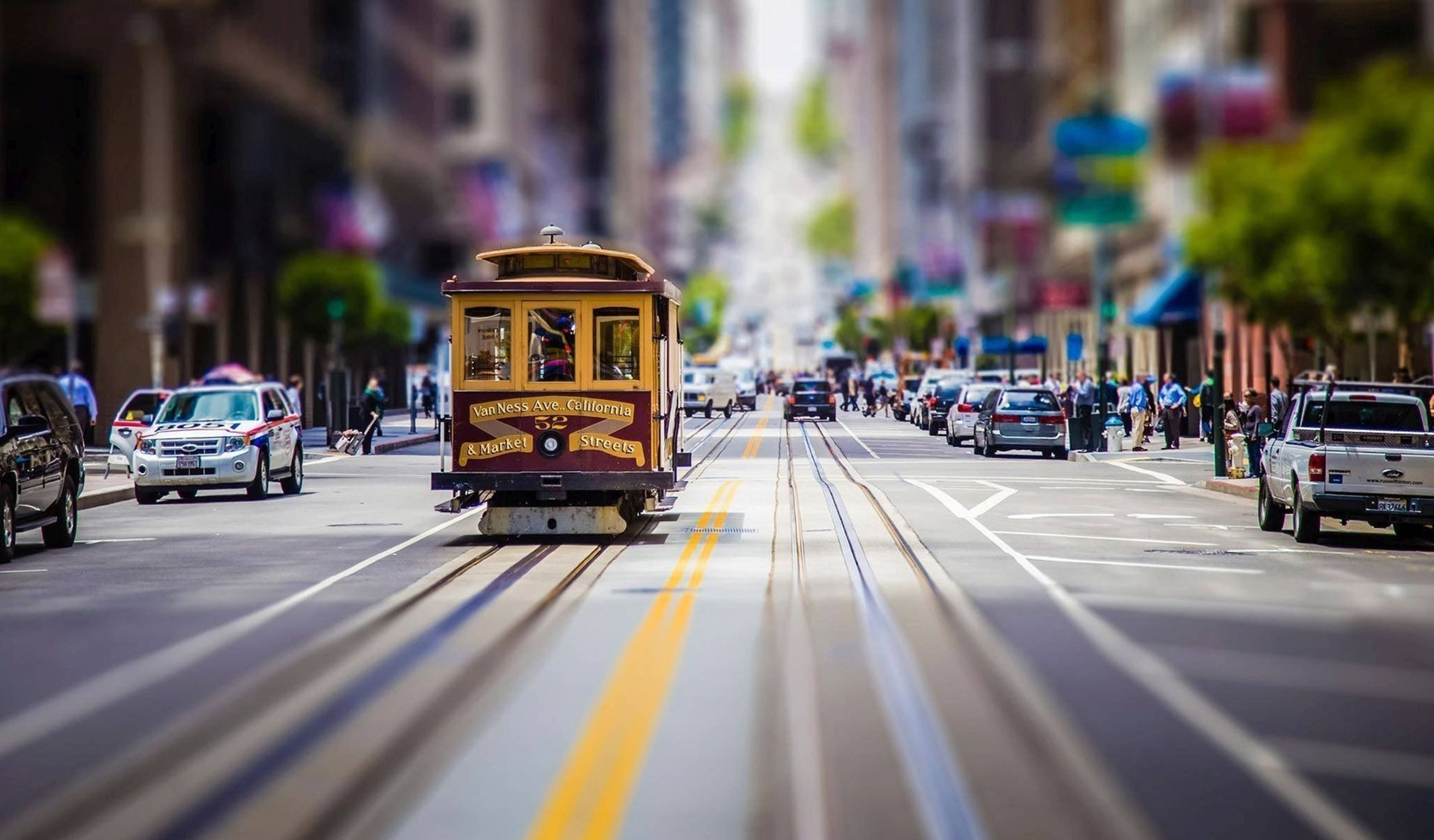 城市景觀 桌布 壁紙 — 一輛經典纜車沿著繁華的城市街道滑行，帶有模糊的動感和充滿活力的都市能量。