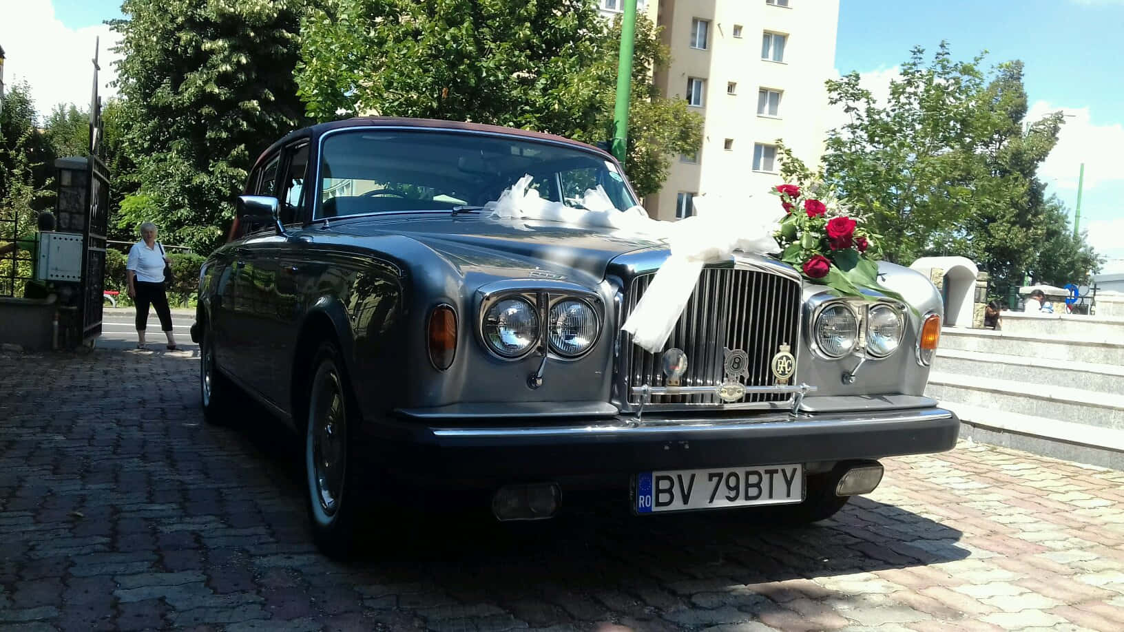 Bentley T2 桌布 壁紙 — 一輛經典銀色賓利婚車，飾有紅玫瑰和白色絲帶，停泊在陽光照耀的鵝卵石街道上。