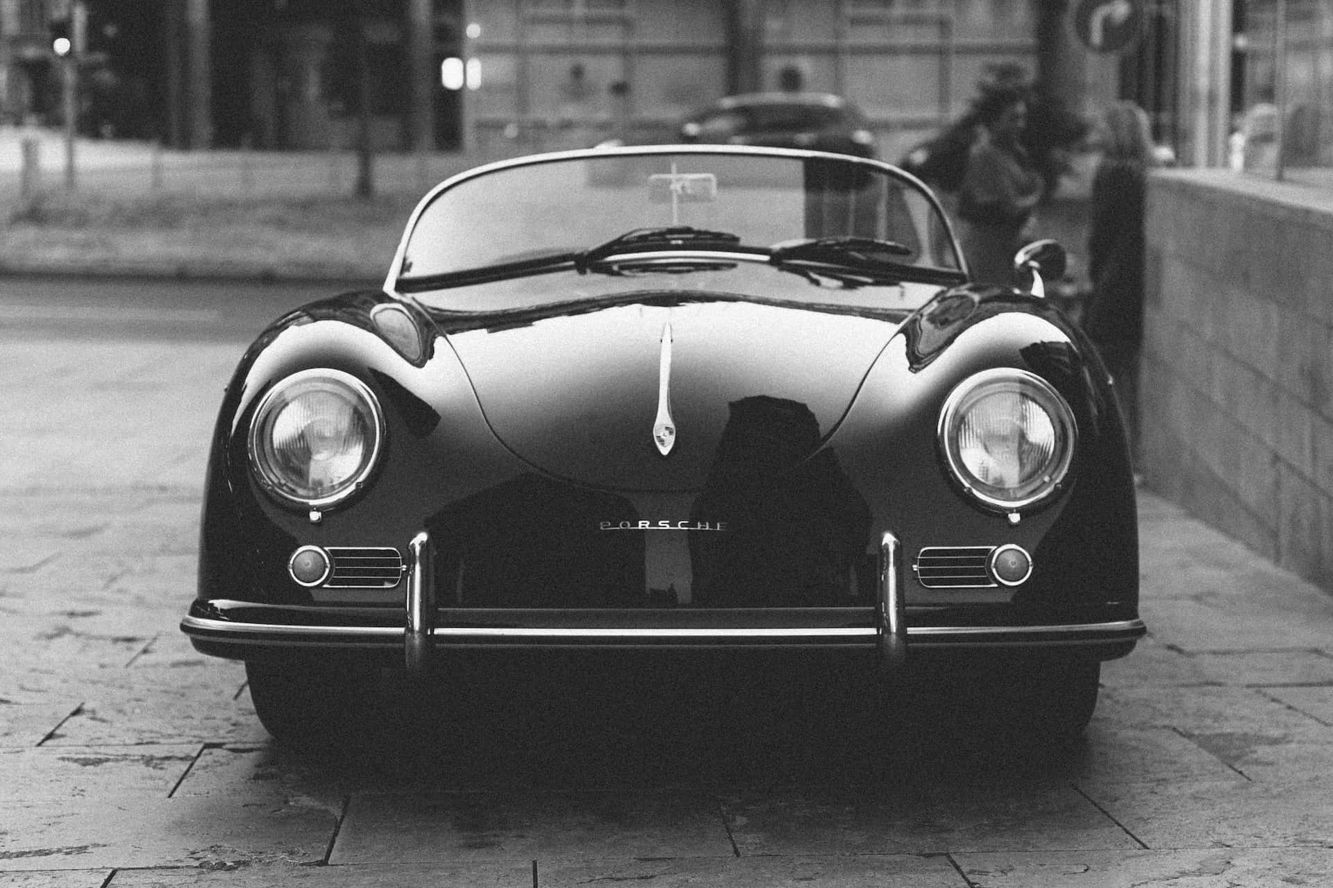 Black And White Car 桌布 壁紙 — 一輛經典黑色保時捷356開篷車停泊在濕漉漉的鵝卵石街道上，以單色呈現，帶有倒影和柔和背景模糊效果。