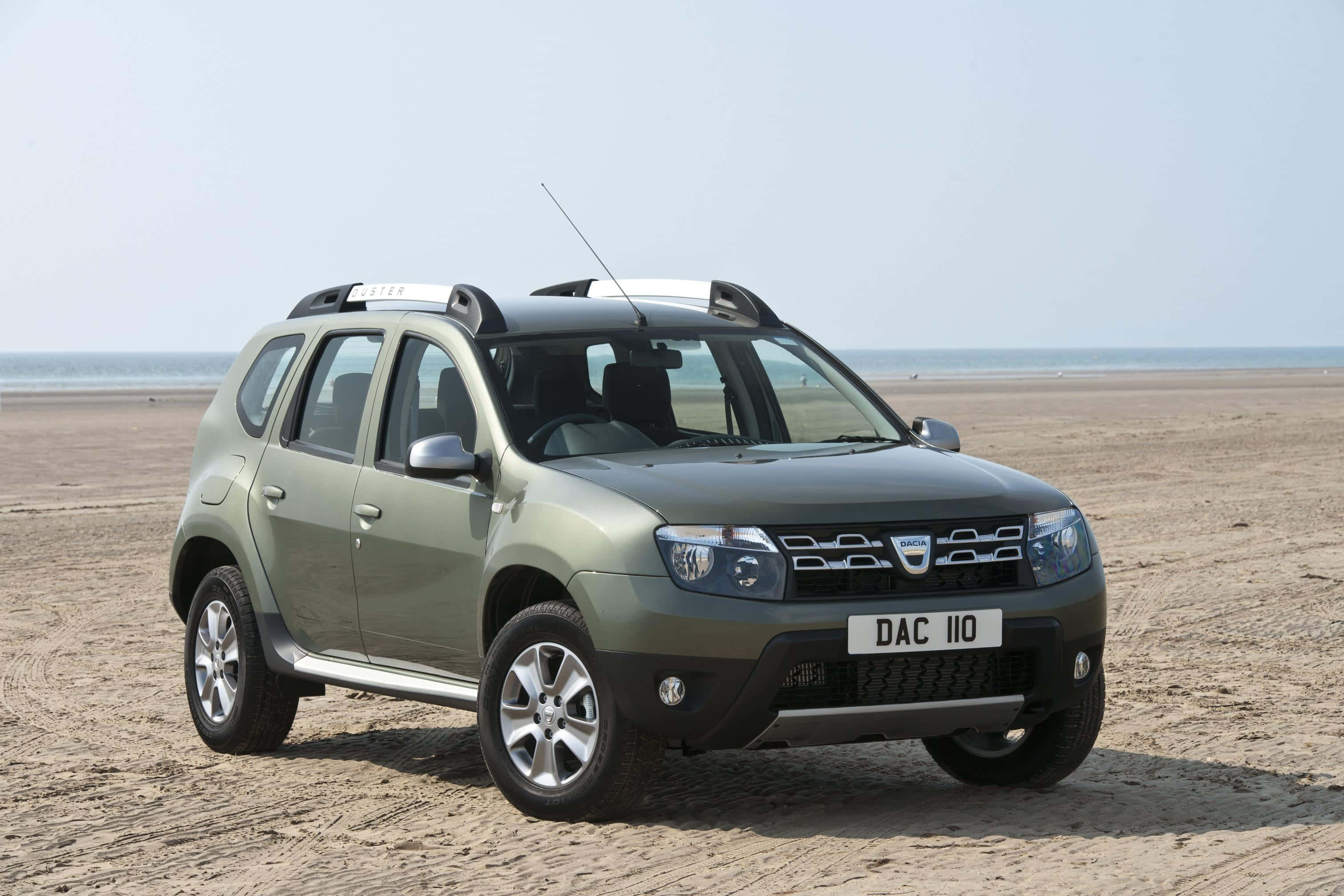 Dacia 桌布 壁紙 — 一輛綠色Dacia Duster SUV停泊在寬闊的沙灘上，背景是海洋和晴朗的天空。