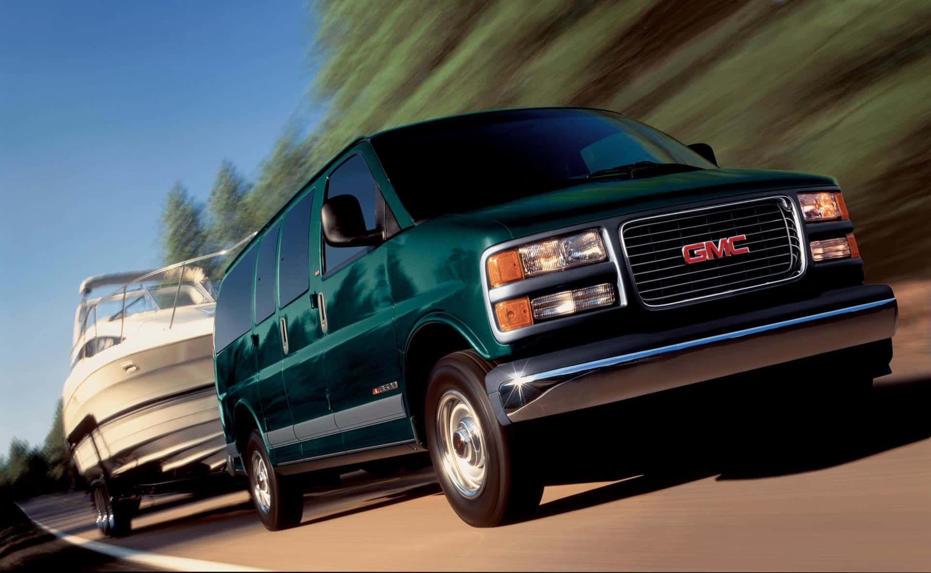 Gmc Savana 桌布 壁紙 — 一輛綠色GMC客貨車在道路上疾馳，拖著一艘白色船隻，背景是模糊的森林。
