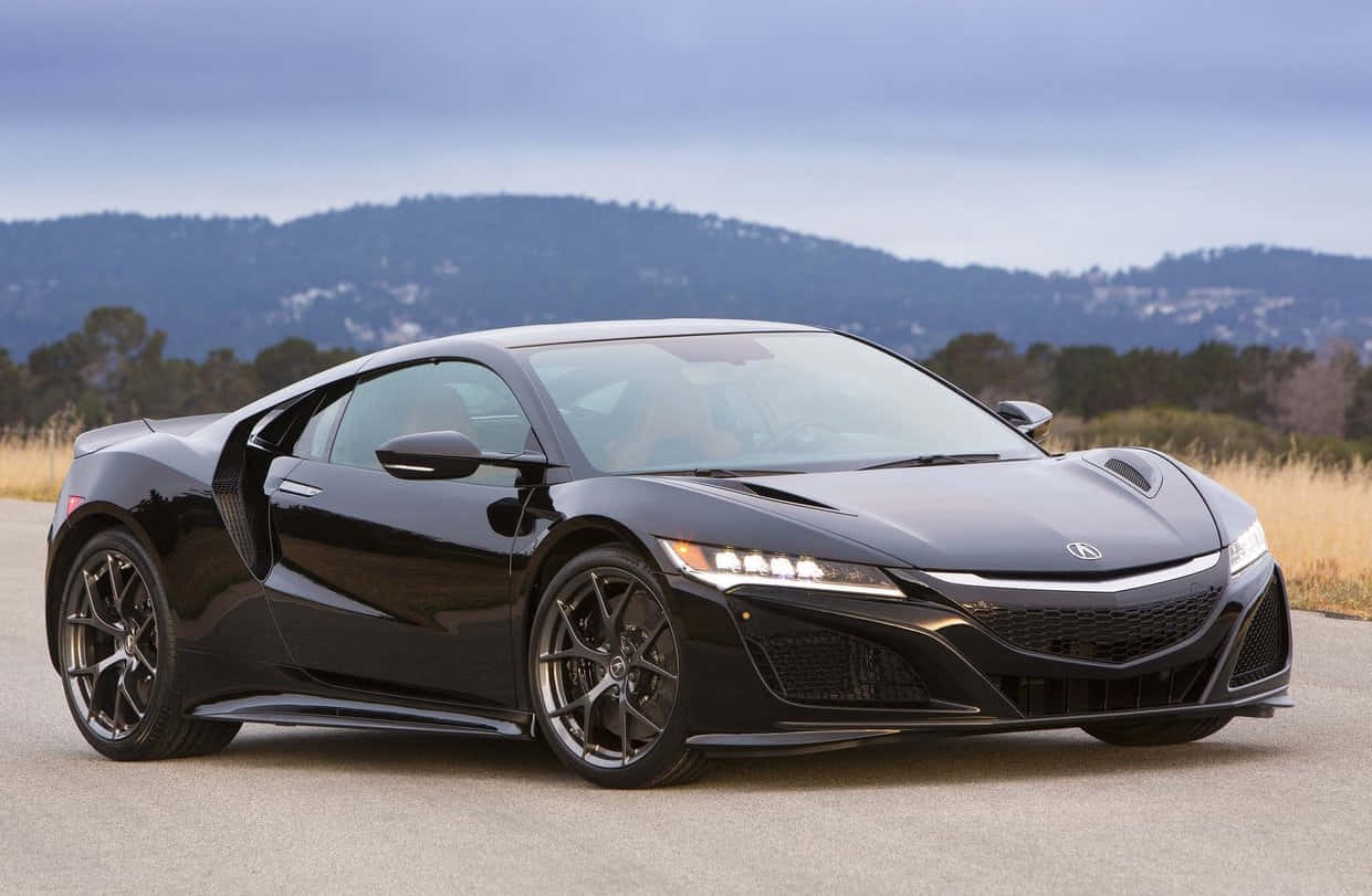 Honda Nsx 桌布 壁紙 — 一輛線條銳利、車燈閃亮的時尚黑色跑車，停泊在鋪砌的道路上，背景是起伏的丘陵和多雲的天空。