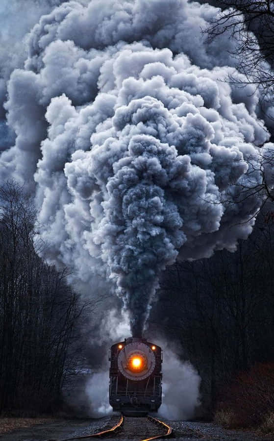 photo 桌布 壁紙 — 一輛蒸汽火車在黃昏時分穿越森林，煙囪噴出巨大的煙霧。