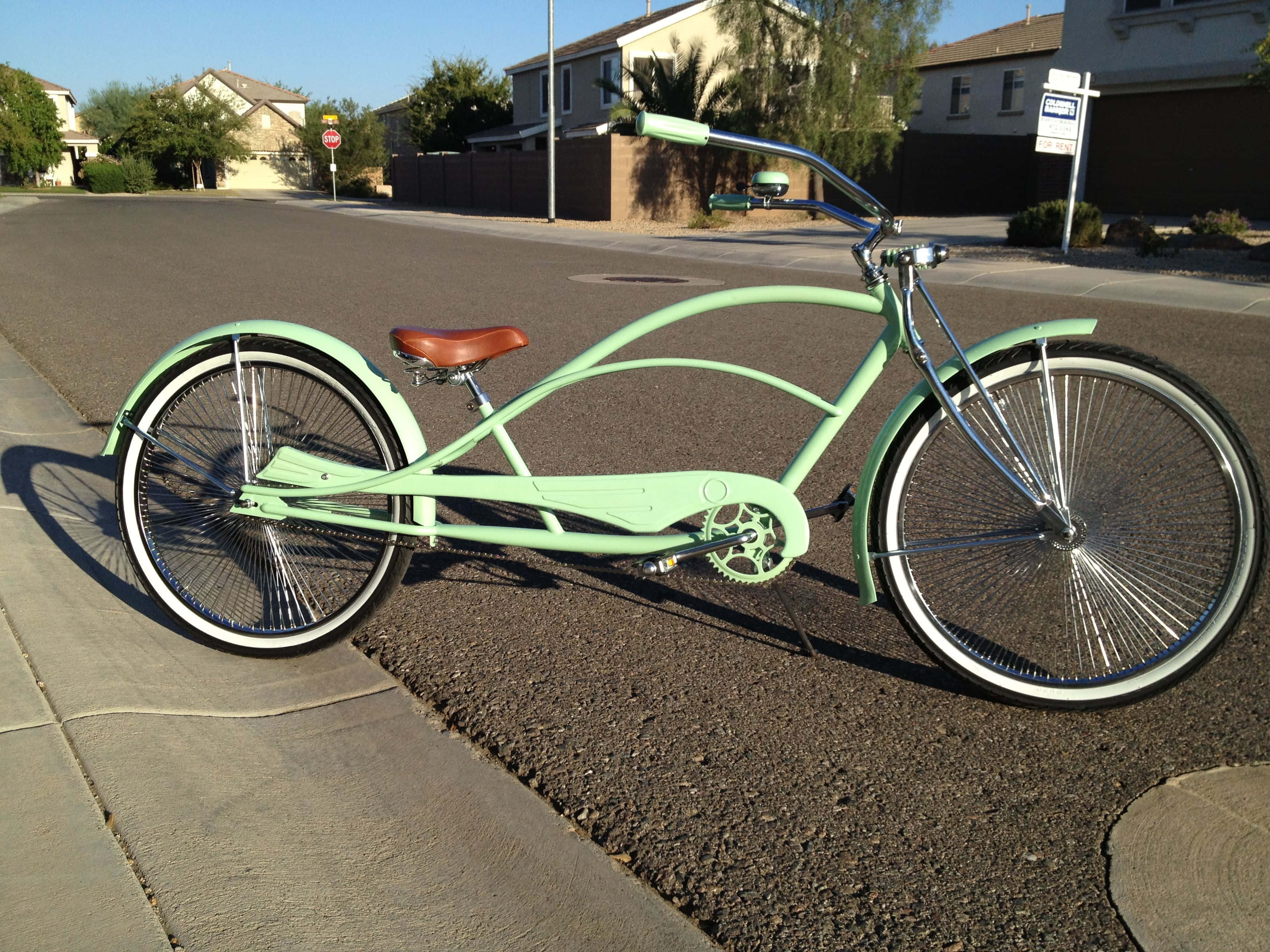 Beach Cruiser 桌布 壁紙 — 一輛薄荷綠復古巡洋艦自行車，帶有鍍鉻裝飾和棕色皮革座椅，停在日出時分的郊區街道上。