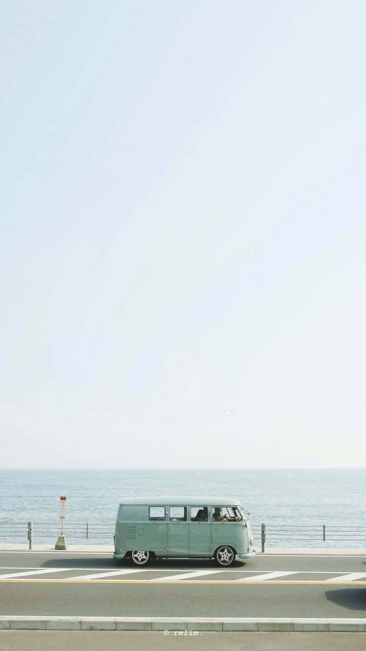 Minimalist Photography 桌布 壁紙 — 一輛薄荷綠色的復古貨車沿著海岸道路行駛，天空朦朧，平靜的海洋延伸至地平線。