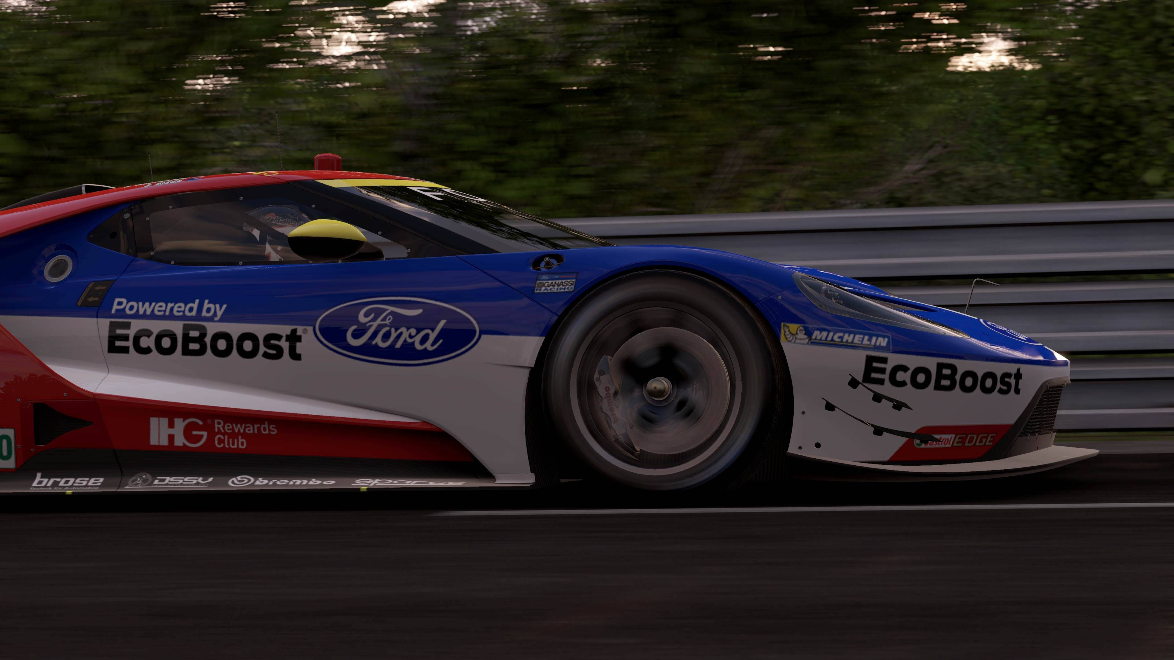 Project Cars 4K Ford GT 壁紙 — 一輛藍、紅、白色的福特GT賽車在賽道上疾馳，背景是模糊的綠色樹木。