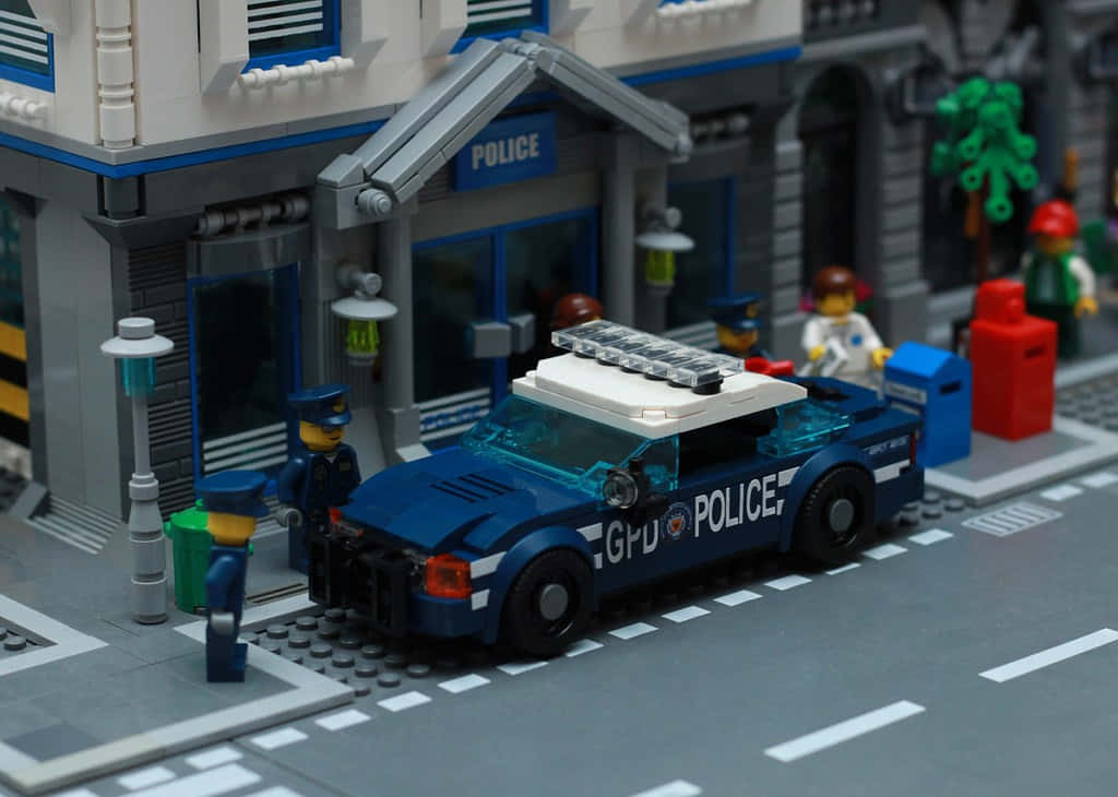 Gotham City Police Department 桌布 壁紙 — 一輛藍色LEGO警車停泊在LEGO警察局外，配有迷你人偶和街道細節。