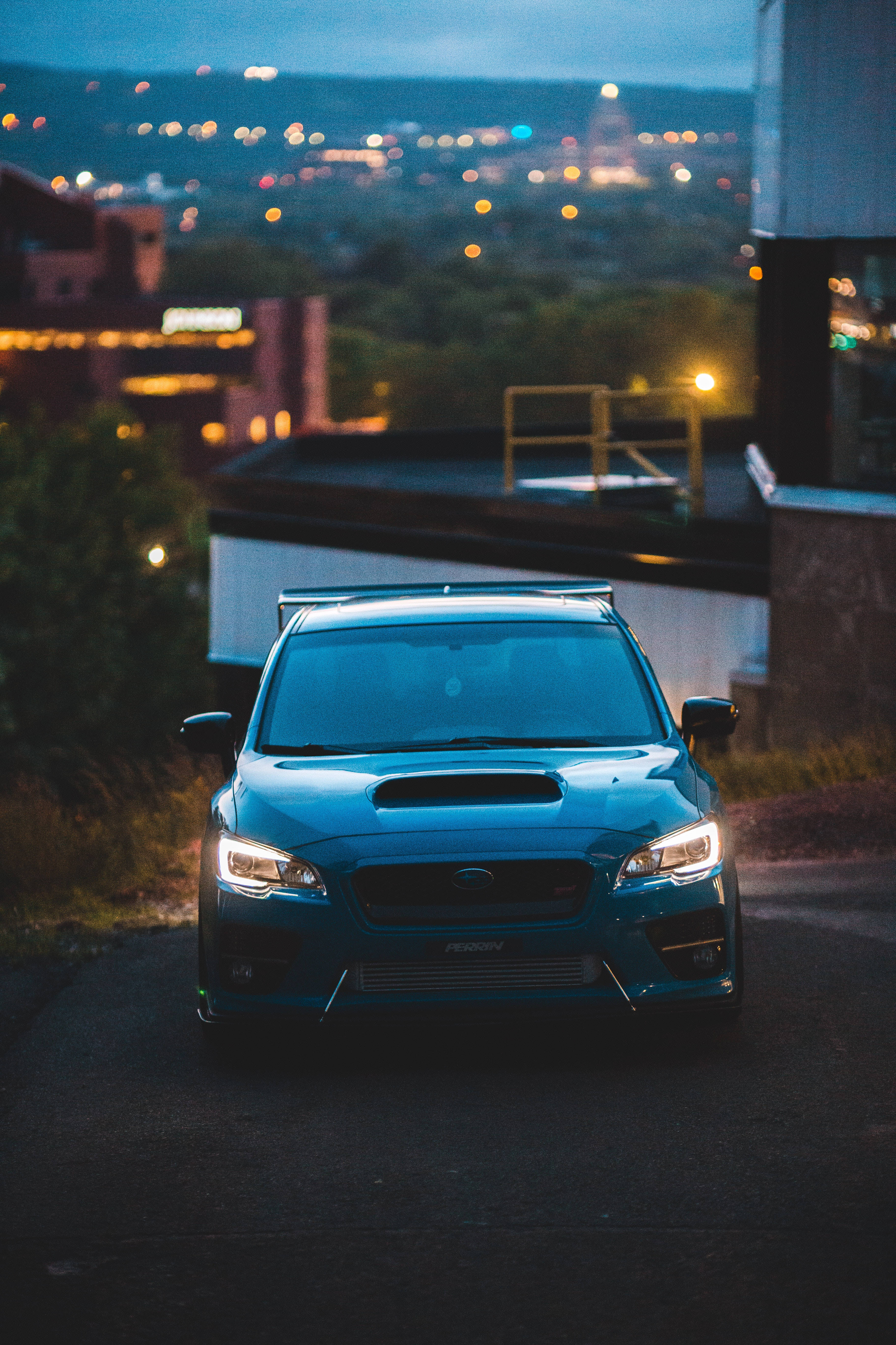 subaru 桌布 壁紙 — 一輛藍色Subaru WRX STI在黃昏時停泊在屋頂上，背景中城市燈光閃爍。
