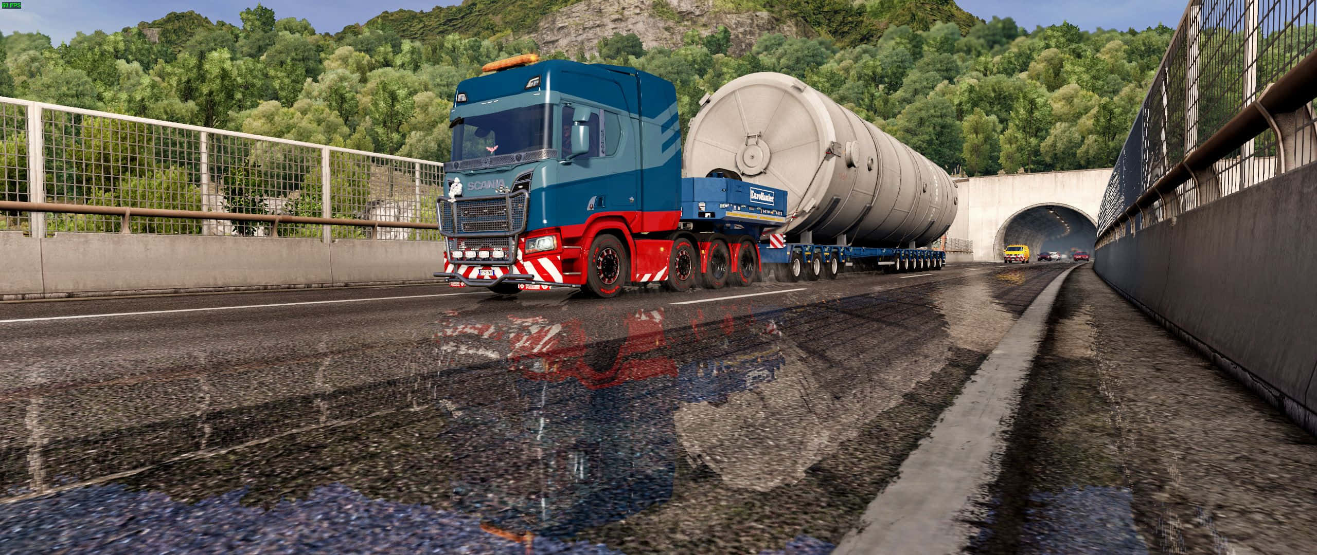 Simulation Games 桌布 壁紙 — 一輛藍色和紅色的半掛卡車拖著一個大型圓柱形油箱，在潮濕的高速公路上駛向被綠色山丘環繞的隧道入口。