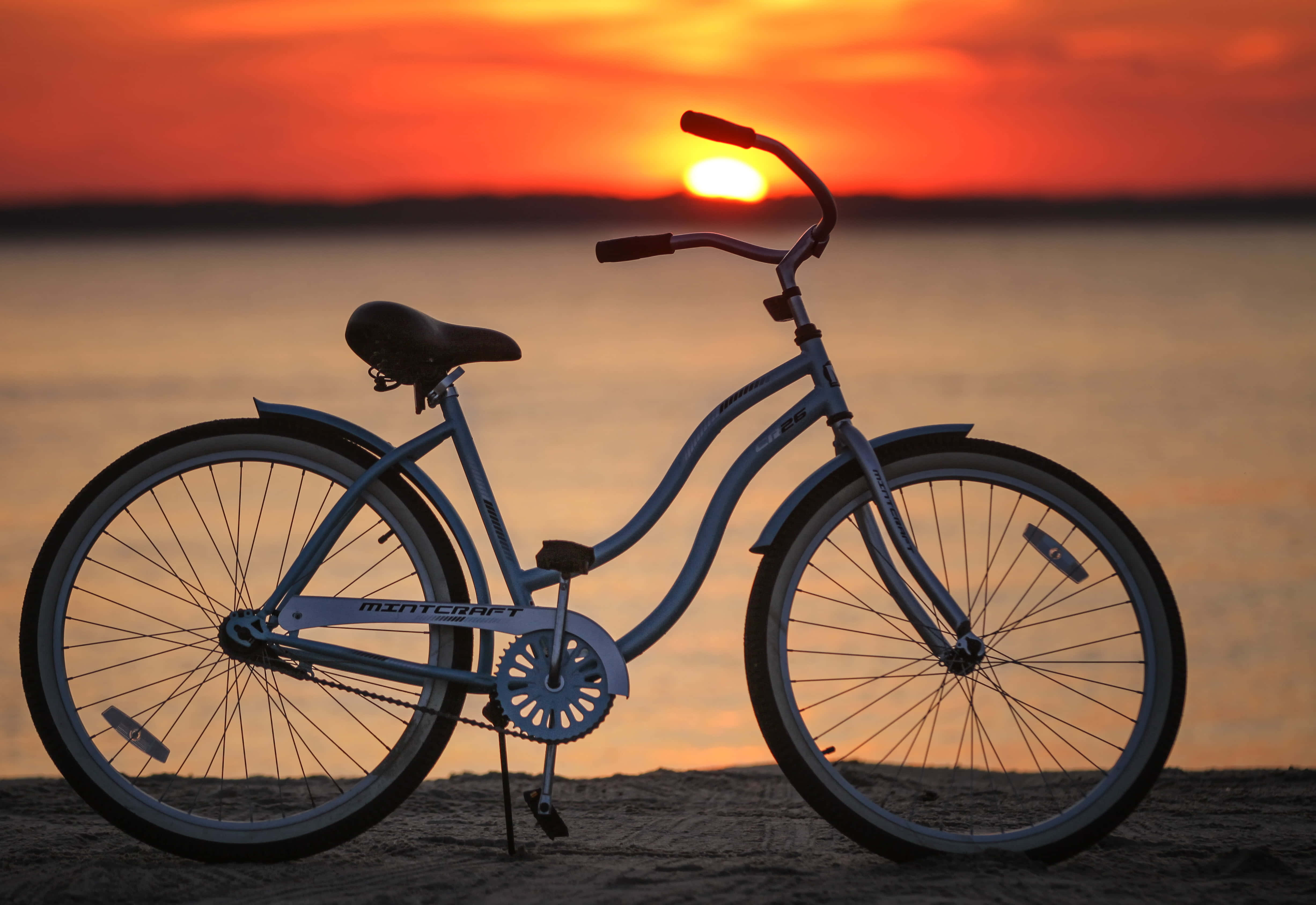 Beach Cruiser 桌布 壁紙 — 一輛藍色單車在海灘上呈現剪影，太陽以火熱的橙色和紅色色調在水面上落下。