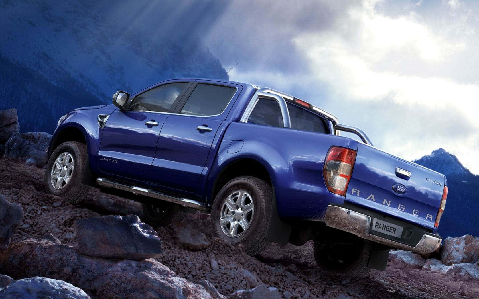 Ford Ranger 桌布 壁紙 — 一輛藍色福特 Ranger 皮卡車在戲劇性的多雲天空下攀爬岩石山徑。