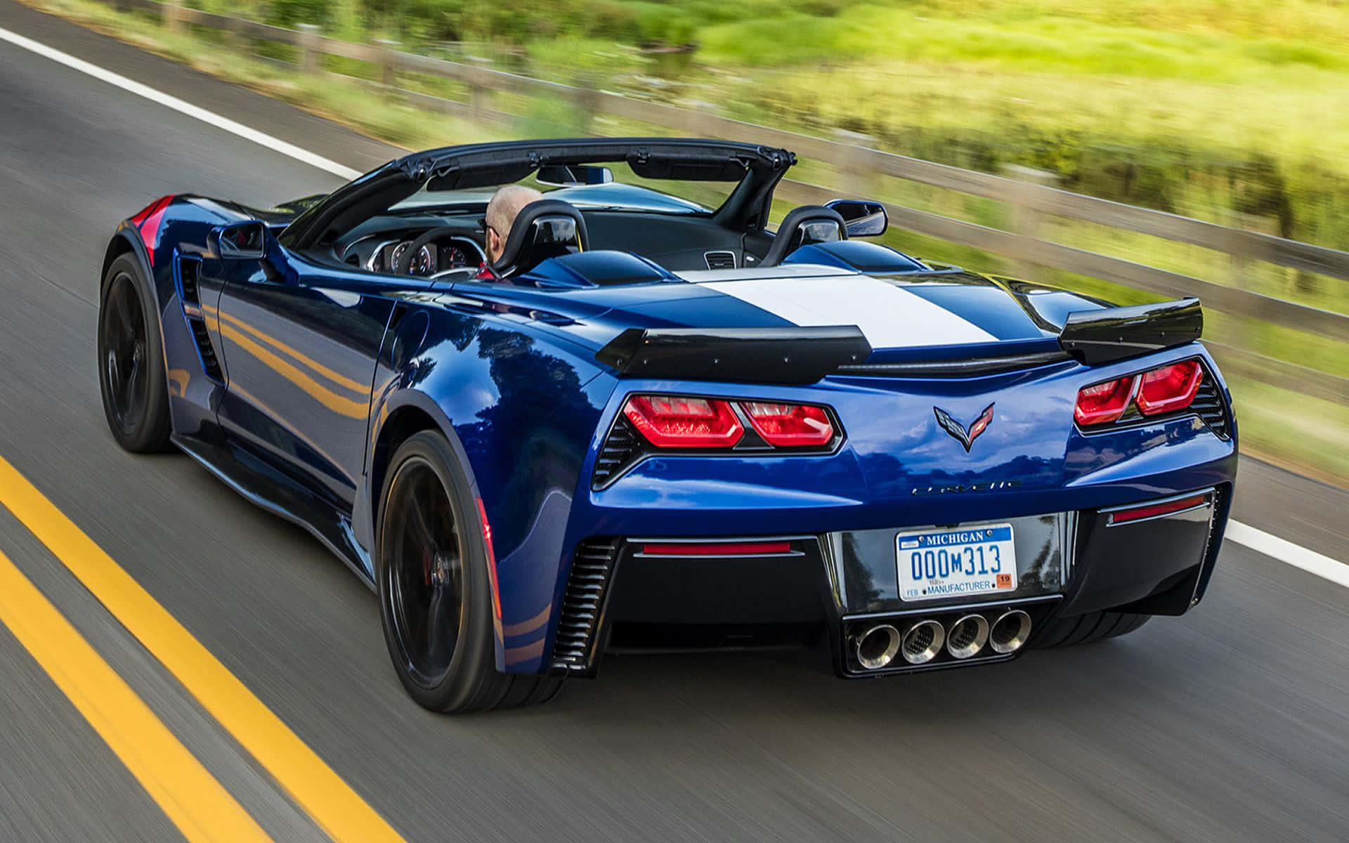 Chevrolet Corvette Grand Sport 桌布 壁紙 — 一輛藍色開篷跑車在陽光明媚的高速公路上飛馳，模糊的綠樹從旁掠過。