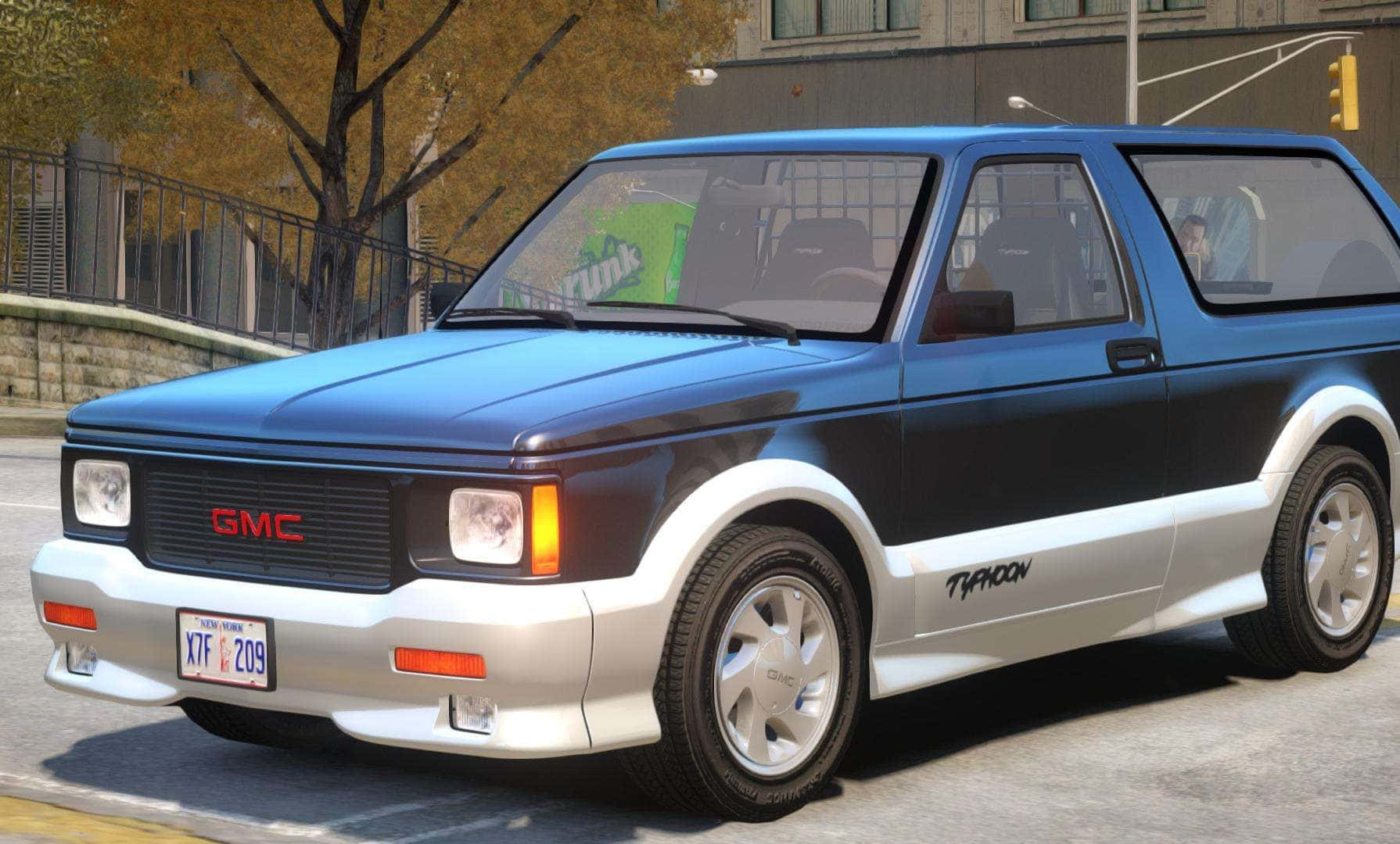 Gmc Typhoon 桌布 壁紙 — 一輛藍銀色GMC Typhoon旅行車停在城市街道上，背景有秋樹和交通燈。