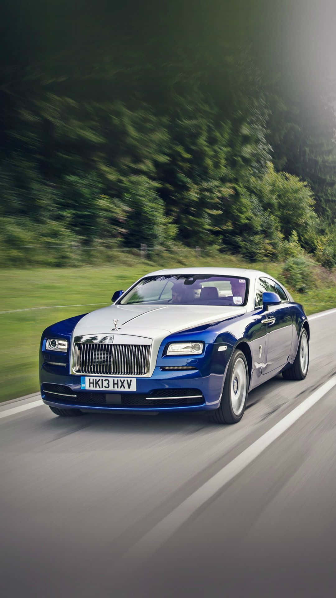 Rolls Royce 桌布 壁紙 — 一輛藍銀色的勞斯萊斯魅影在蜿蜒的道路上疾馳，穿過茂密的綠色森林，帶有動態模糊效果。